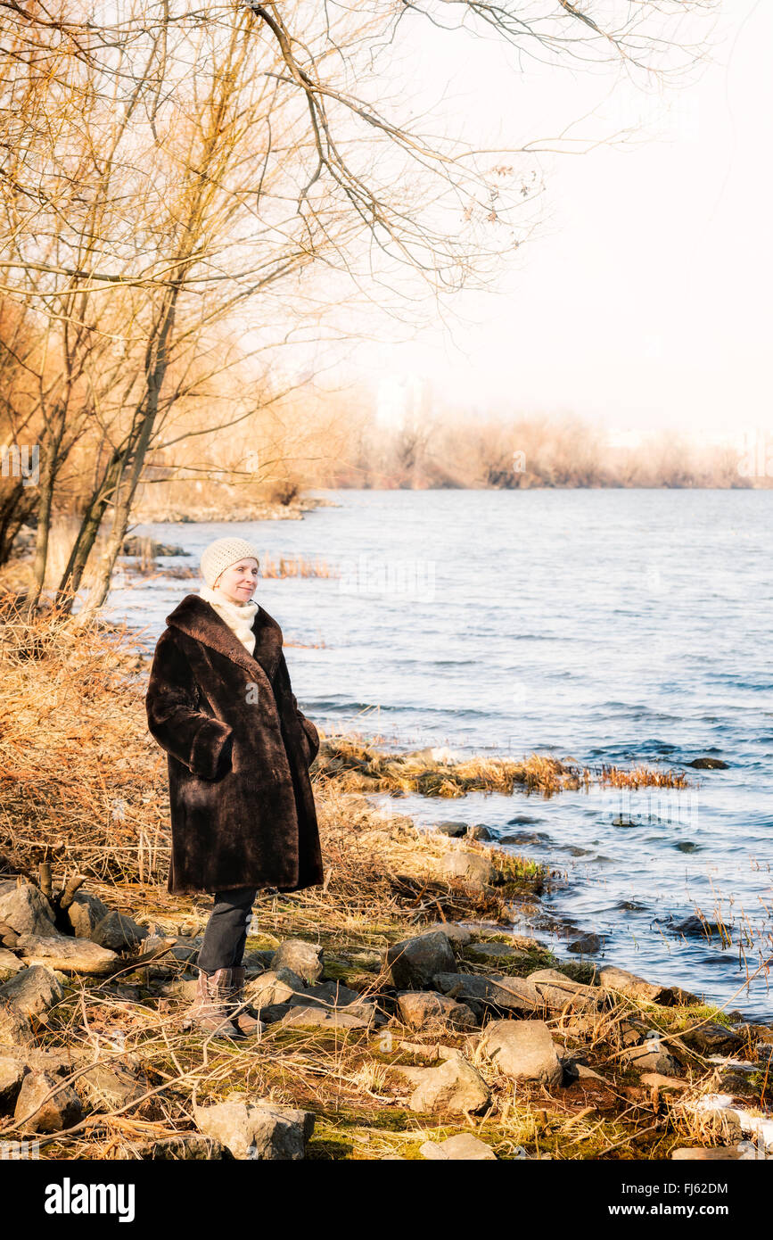 Una donna matura che indossa una calda pelliccia e un cappello di lana resta vicino al fiume Dnieper a Kiev, Ucraina, durante la stagione invernale Foto Stock