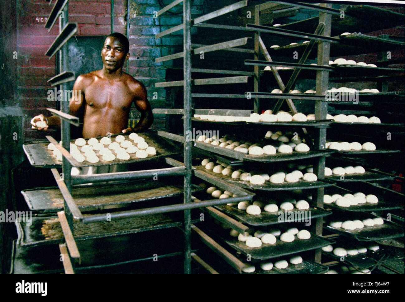 Il panettiere cubano Alexei Suarez nel panificio, tenendo il vassoio da forno con baps, Cuba Foto Stock