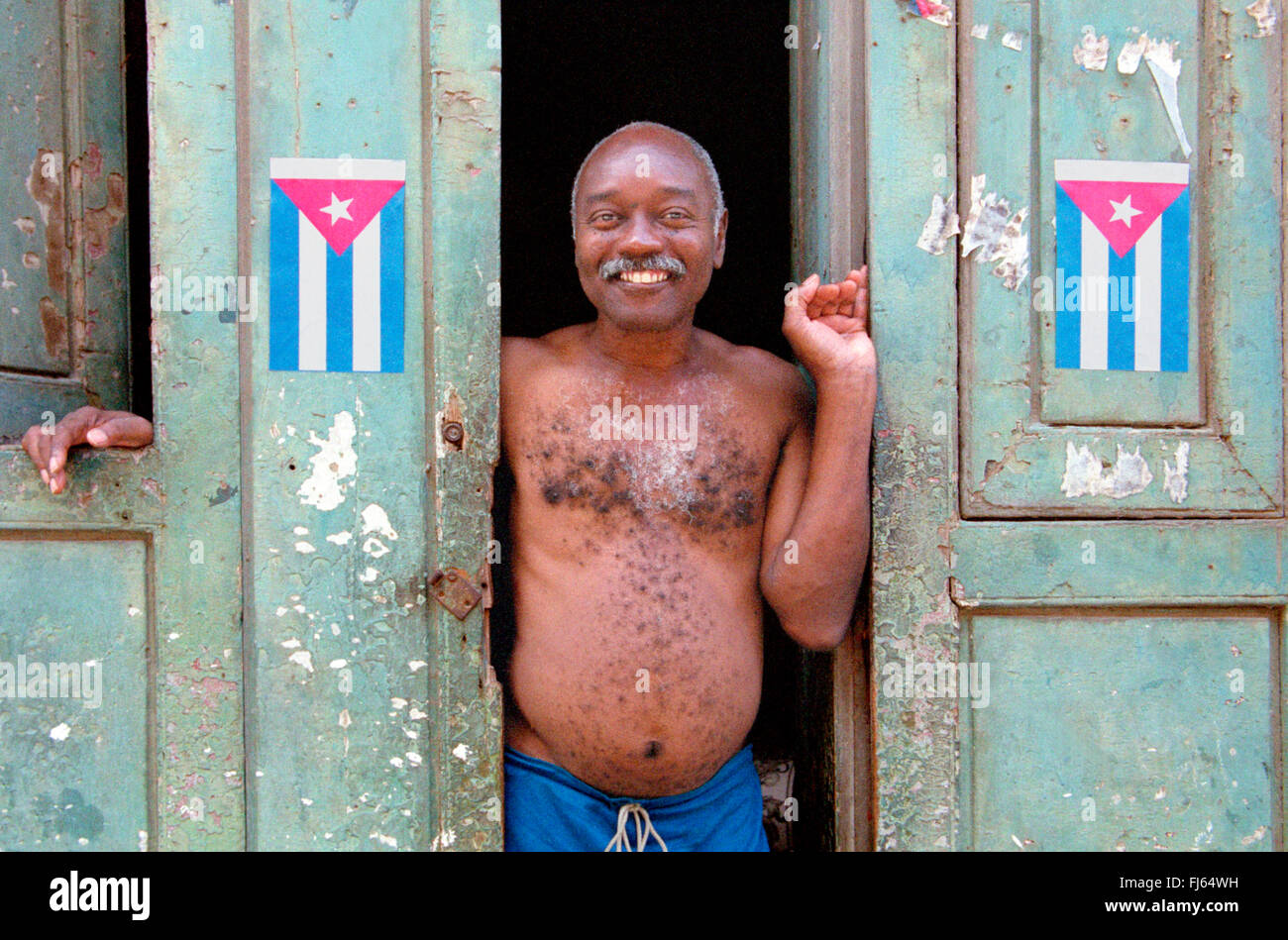 Uomo cubano in piedi nella porta di ingresso, con bandiere cubane a lato, Cuba Foto Stock