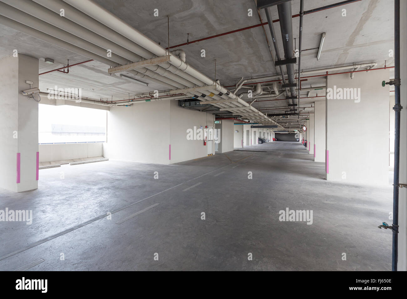 Lo spazio vuoto dell'area di parcheggio all'interno di edificio pubblico che ha molti tubi di acqua installati sul soffitto. Foto Stock