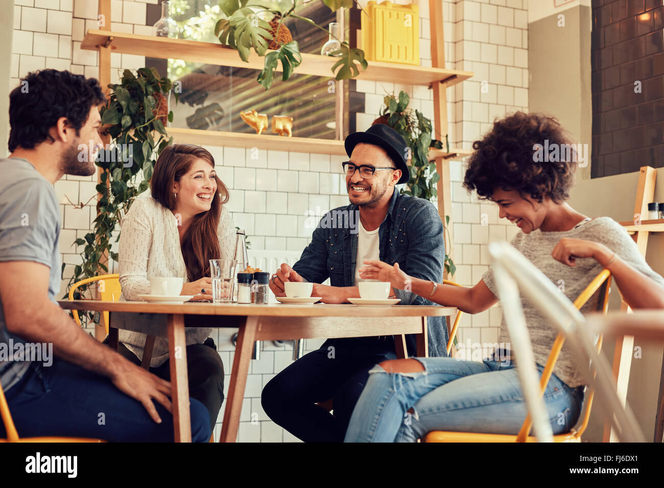 Gruppo di amici di godere in cafe insieme. I giovani riuniti in un cafe'. Giovani uomini e donne seduti al tavolo del bar e smilin Foto Stock