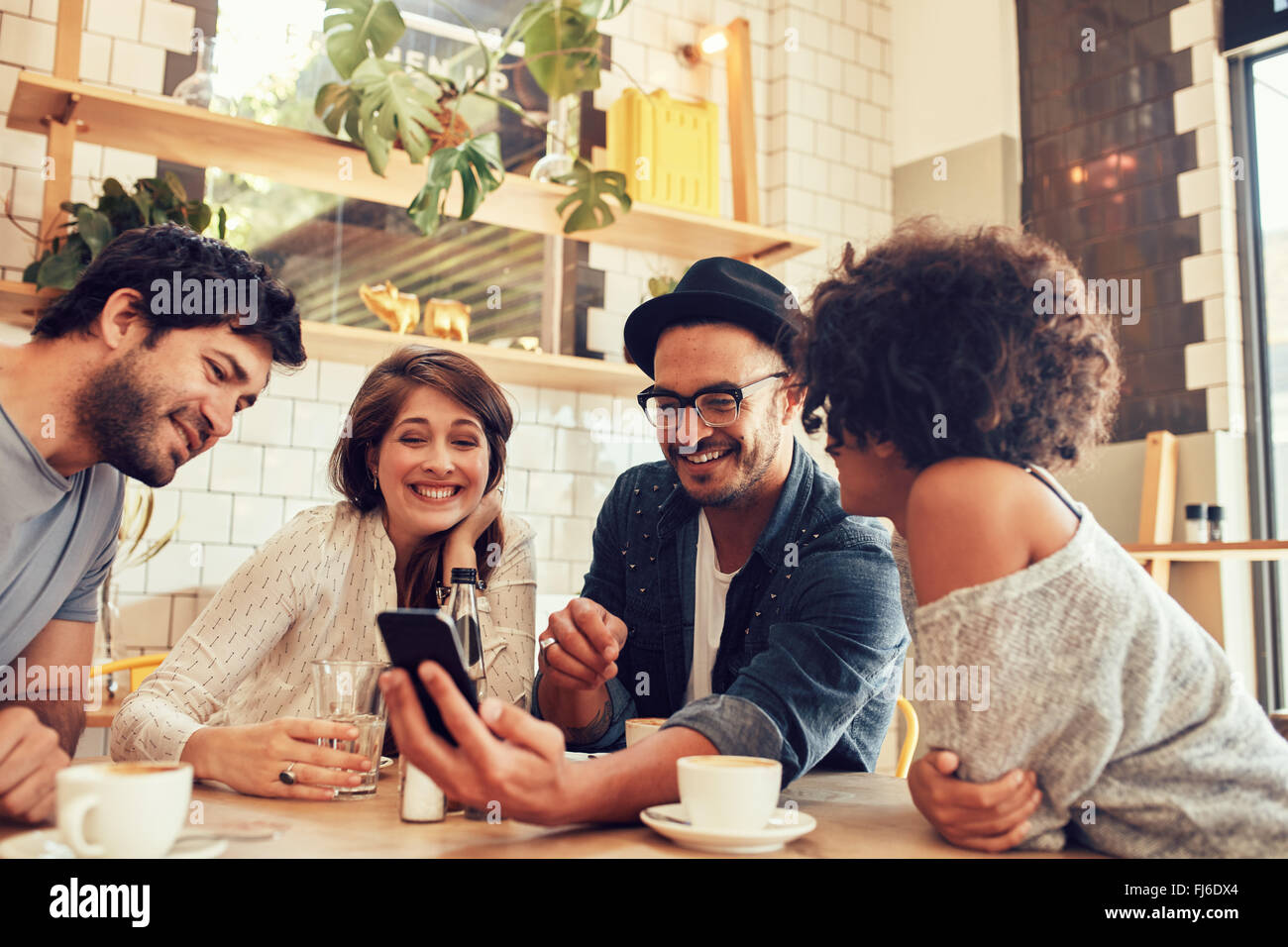Ritratto di un gruppo di giovani amici riuniti in un cafe e guardando le foto sul telefono cellulare. Giovani uomini e donne seduti a Foto Stock