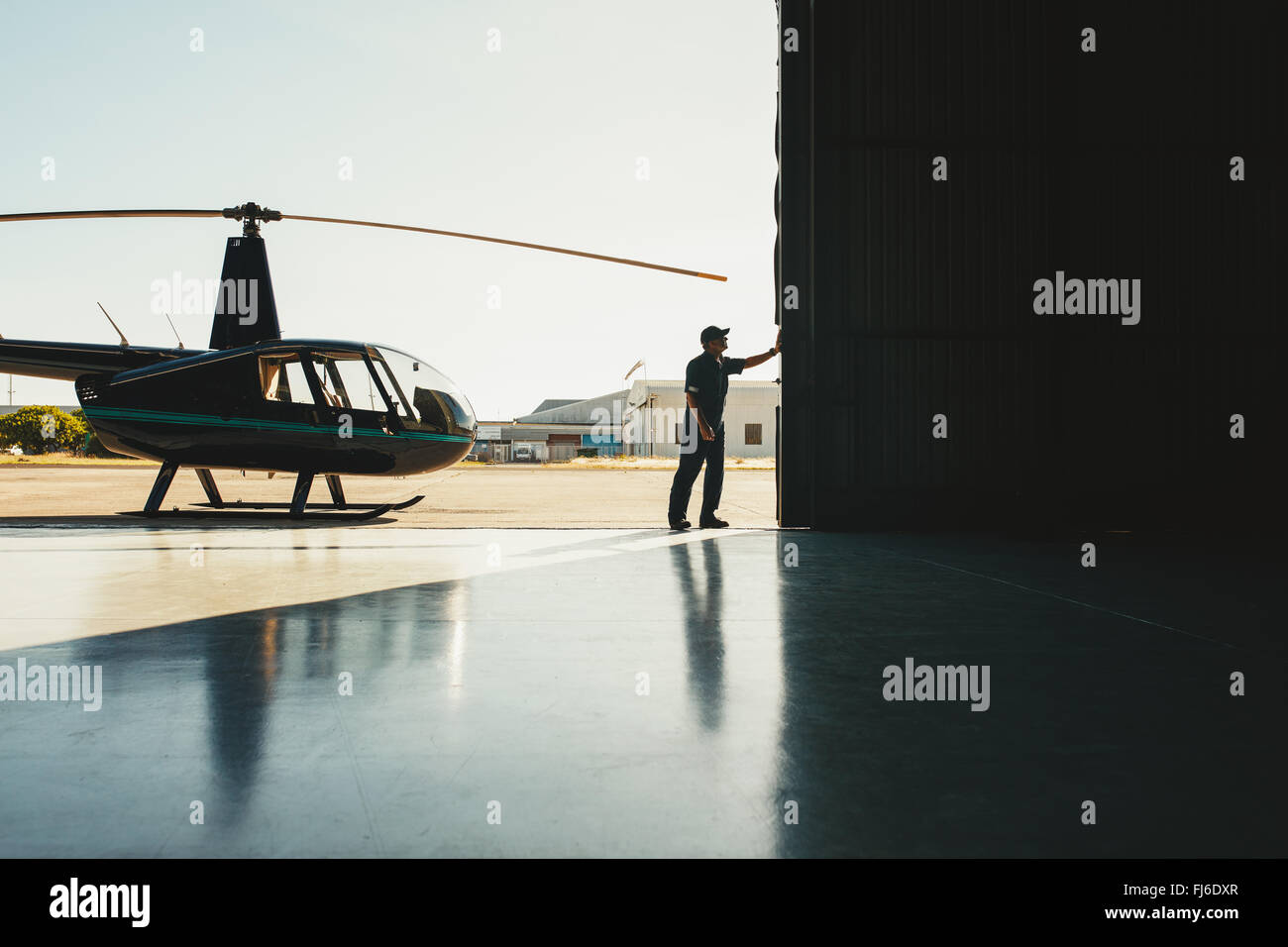 Mechanic aprendo la porta di un hangar aereo con un elicottero Foto Stock