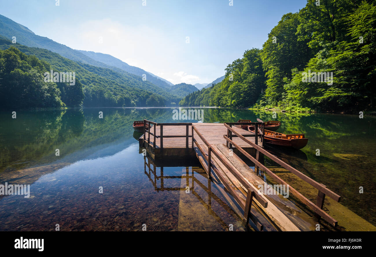 Calma acqua di lago con riflessioni di foresta sulle colline e bellissimo vecchio molo in legno Foto Stock