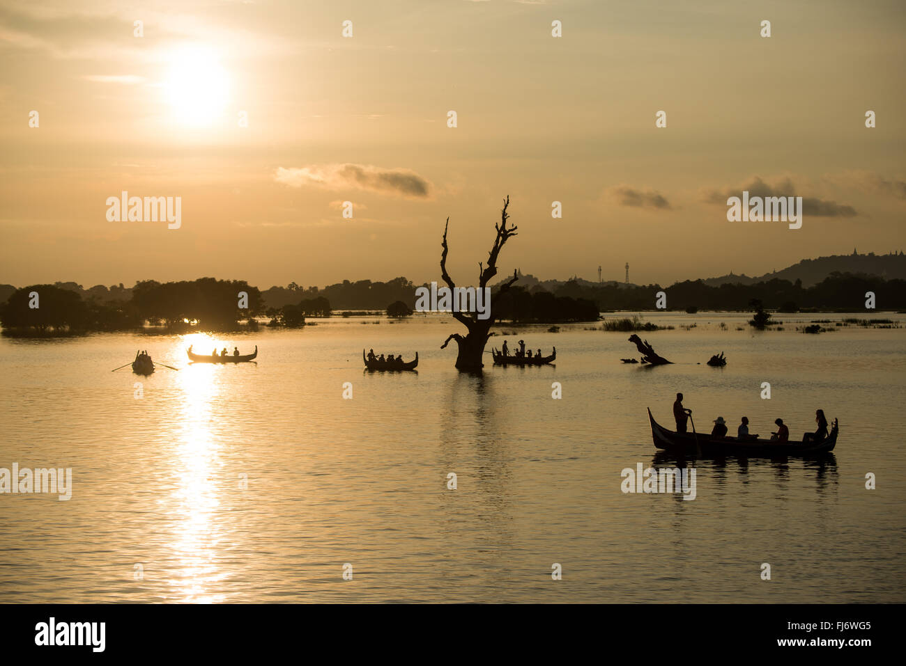 Barche sul lago Taungthaman Mandalay Myanmar // LAGO TAUNGTHAMAN, Myanmar — sagome di barche e vecchi tronchi di alberi emergono dal lago Taungthaman, un corpo idrico stagionale situato nella città di Amarapura, 11 chilometri a sud-ovest di Mandalay. Il lago ha guadagnato importanza durante la dinastia Konbaung (1752-1885) e si collega al sistema fluviale Ayeyarwady (noto anche come Irrawaddy). L'area è attraversata dal ponte U Bein di 1,2 chilometri, costruito tra il 1849-1851 utilizzando teak recuperato dal Palazzo Inwa smantellato. Il vicino monastero di Mahagandayon, fondato nel 1908, ospita oltre 1.300 monaci Foto Stock