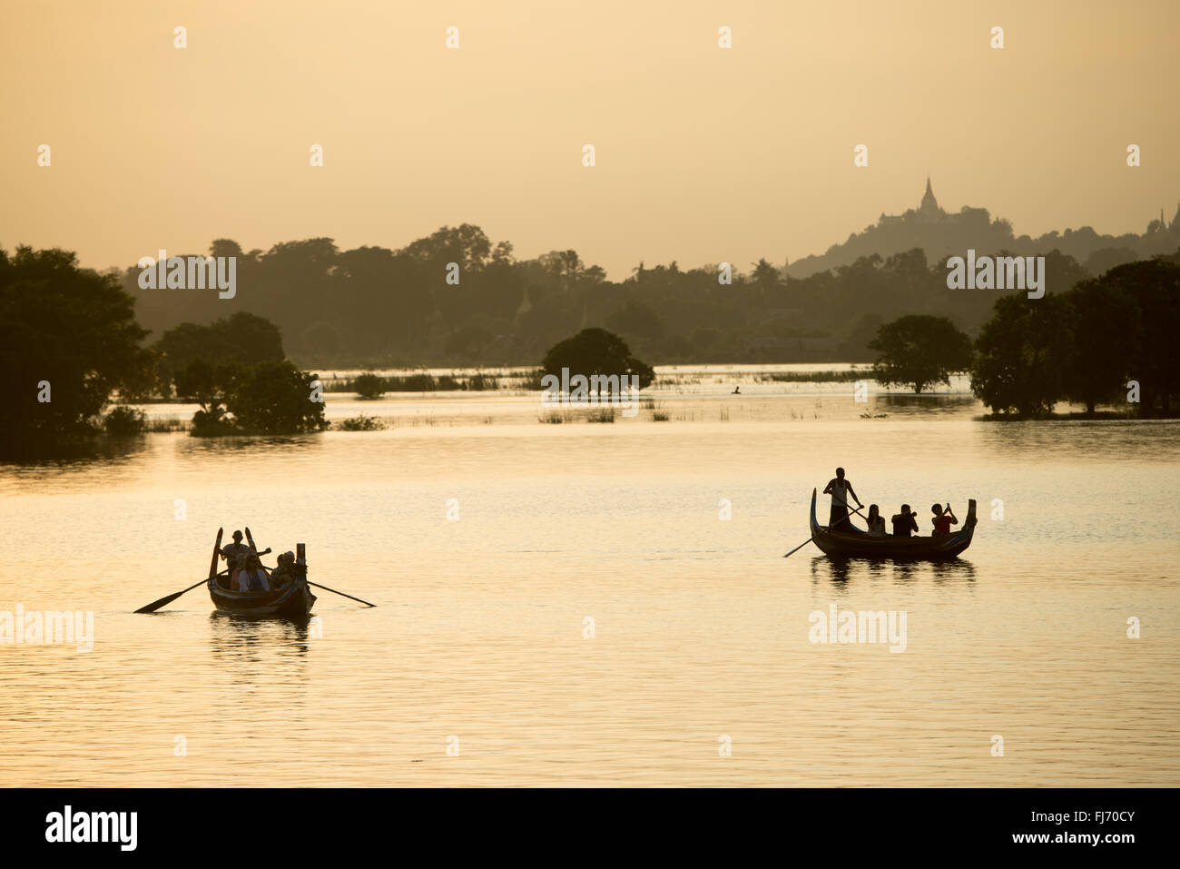 Barche sul lago Taungthaman Amarapura Myanmar // LAGO TAUNGTHAMAN, Myanmar — sagome di barche e vecchi tronchi di alberi emergono dal lago Taungthaman, un corpo idrico stagionale situato nella città di Amarapura, 11 chilometri a sud-ovest di Mandalay. Il lago ha guadagnato importanza durante la dinastia Konbaung (1752-1885) e si collega al sistema fluviale Ayeyarwady (noto anche come Irrawaddy). L'area è attraversata dal ponte U Bein di 1,2 chilometri, costruito tra il 1849-1851 utilizzando teak recuperato dal Palazzo Inwa smantellato. Il vicino monastero di Mahagandayon, fondato nel 1908, ospita oltre 1.300 limoni Foto Stock
