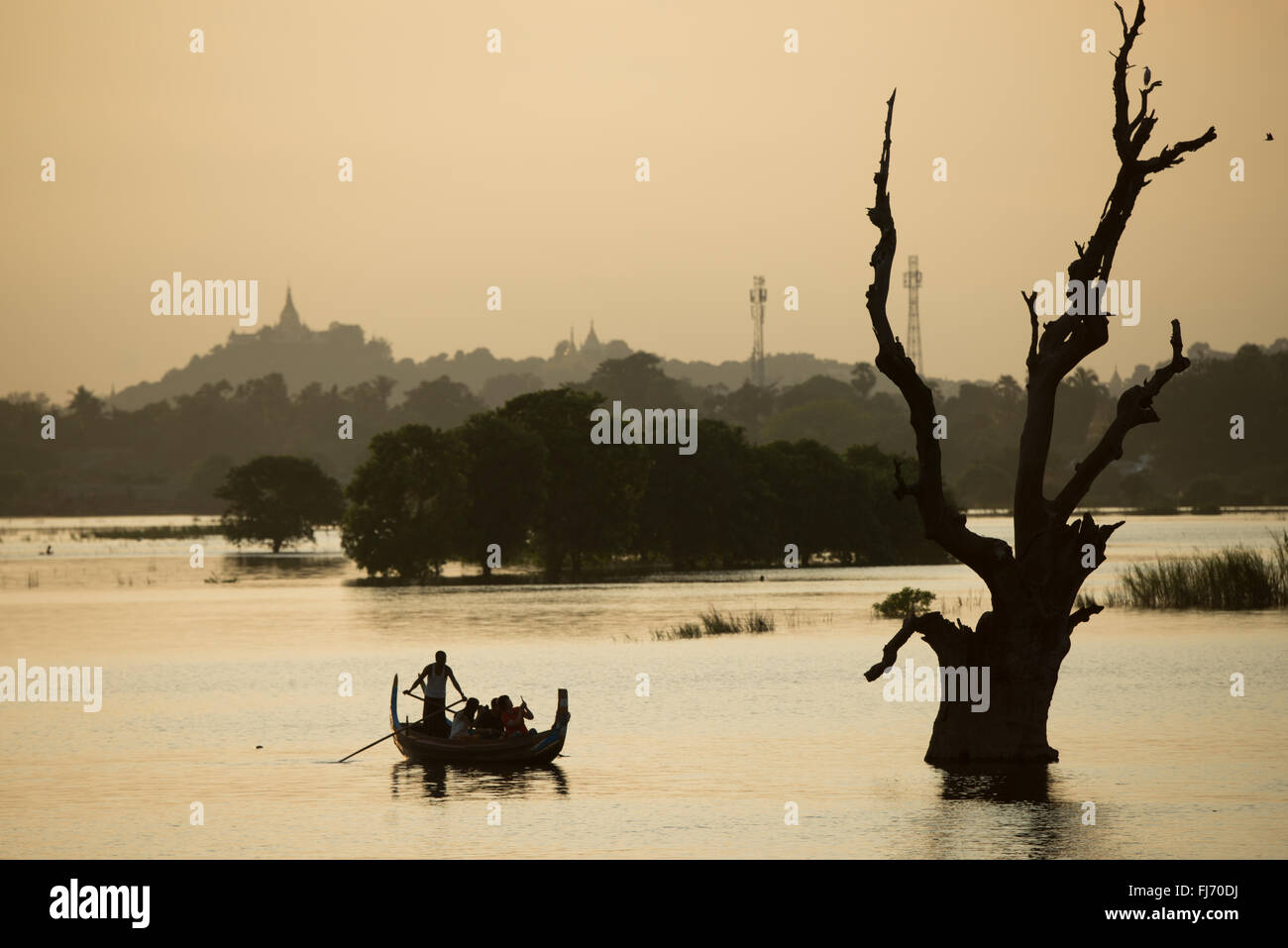 Taungthaman Lake Boats and Tree Trunks Mandalay Myanmar // TAUNGTHAMAN Lake, Myanmar — sagome di barche e vecchi tronchi d'albero emergono dal lago Taungthaman, un corpo idrico stagionale situato nella città di Amarapura, 11 chilometri a sud-ovest di Mandalay. Il lago ha guadagnato importanza durante la dinastia Konbaung (1752-1885) e si collega al sistema fluviale Ayeyarwady (noto anche come Irrawaddy). L'area è attraversata dal ponte U Bein di 1,2 chilometri, costruito tra il 1849-1851 utilizzando teak recuperato dal Palazzo Inwa smantellato. Il vicino monastero di Mahagandayon, fondato nel 1908, ospita ov Foto Stock