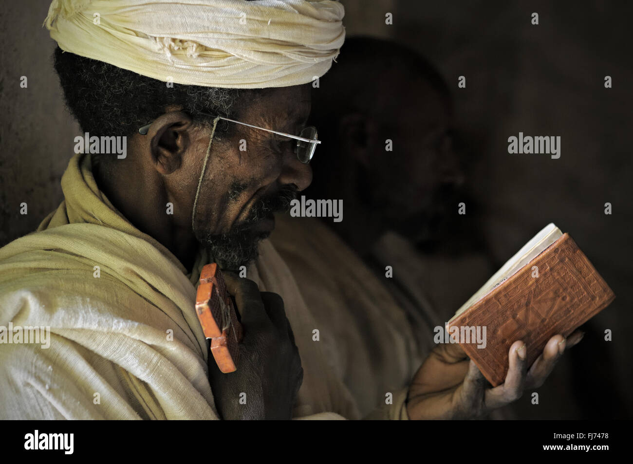 Sacerdote ortodosso tenendo una croce e la lettura di libro sacro all'interno di Mikael Milhaizengi rupestri chiesa nel Tigray, Etiopia Foto Stock