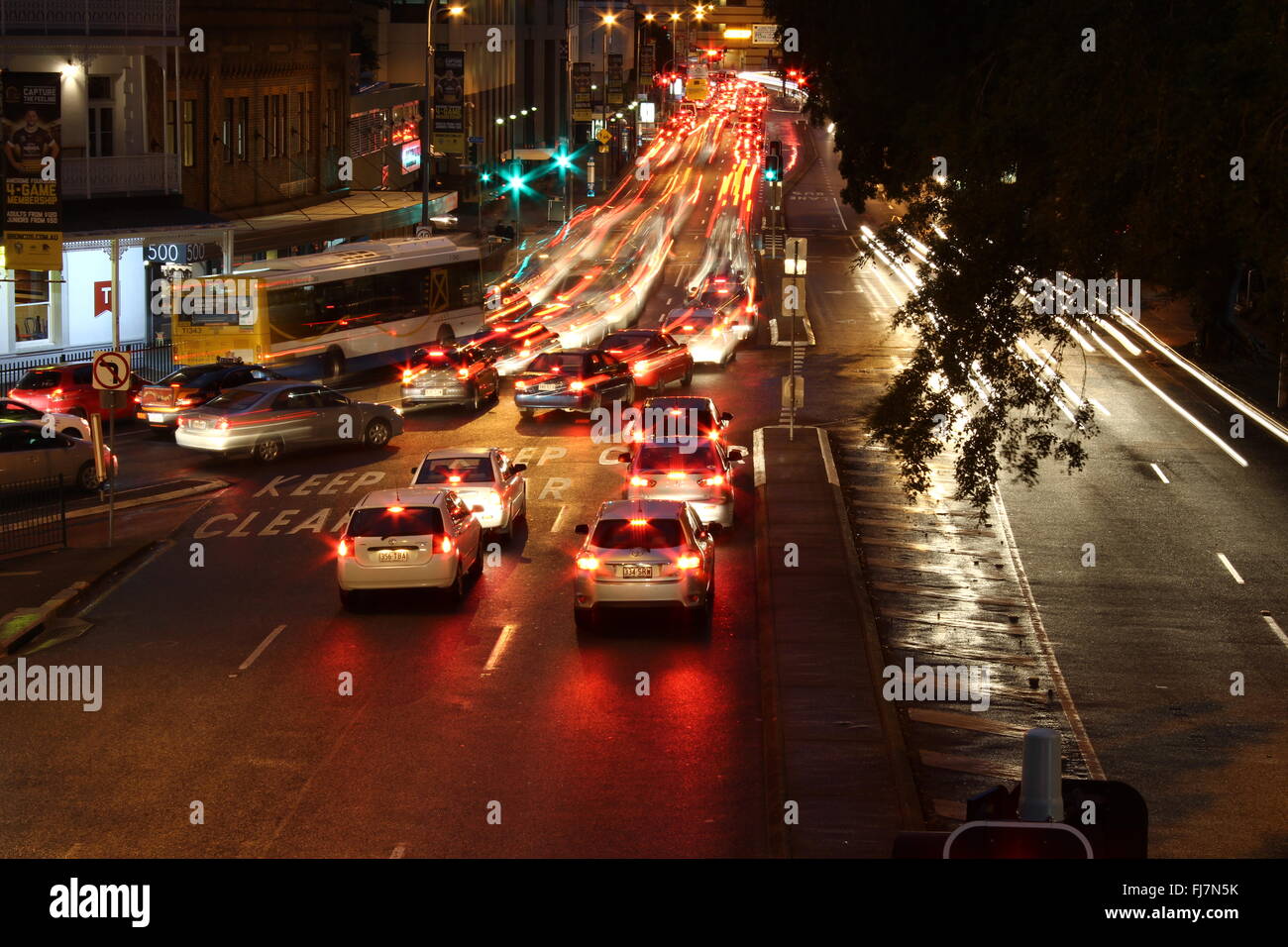 Di sera la città interna traffico dell'ora di punta in condizioni di bagnato in elevazione con percorsi di luce del traffico sul lato sinistro della strada Foto Stock
