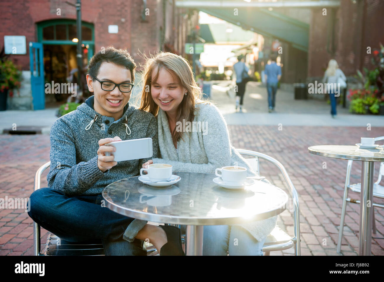 Due sorridenti giovani cercando in smartphone seduti a un tavolo in outdoor cafe Foto Stock