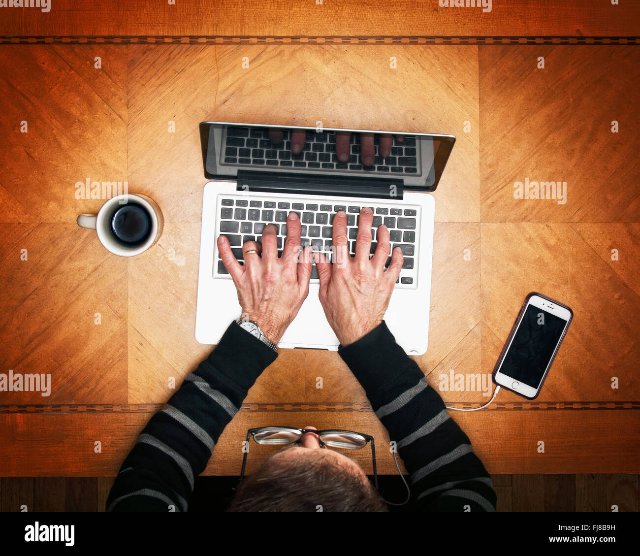 Man digitando su laptop con un telefono cellulare e caffè Foto Stock