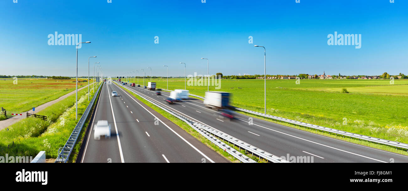 Un'autostrada con il traffico attraverso i campi erbosi su una luminosa e soleggiata giornata nei Paesi Bassi. Foto Stock