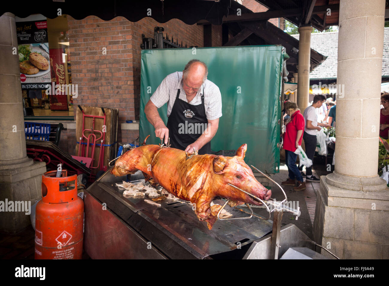 Un uomo del taglio della carne da un arrosto di maiale allo spiedo, Stroud Mercato Agricolo, Gloucestershire Foto Stock