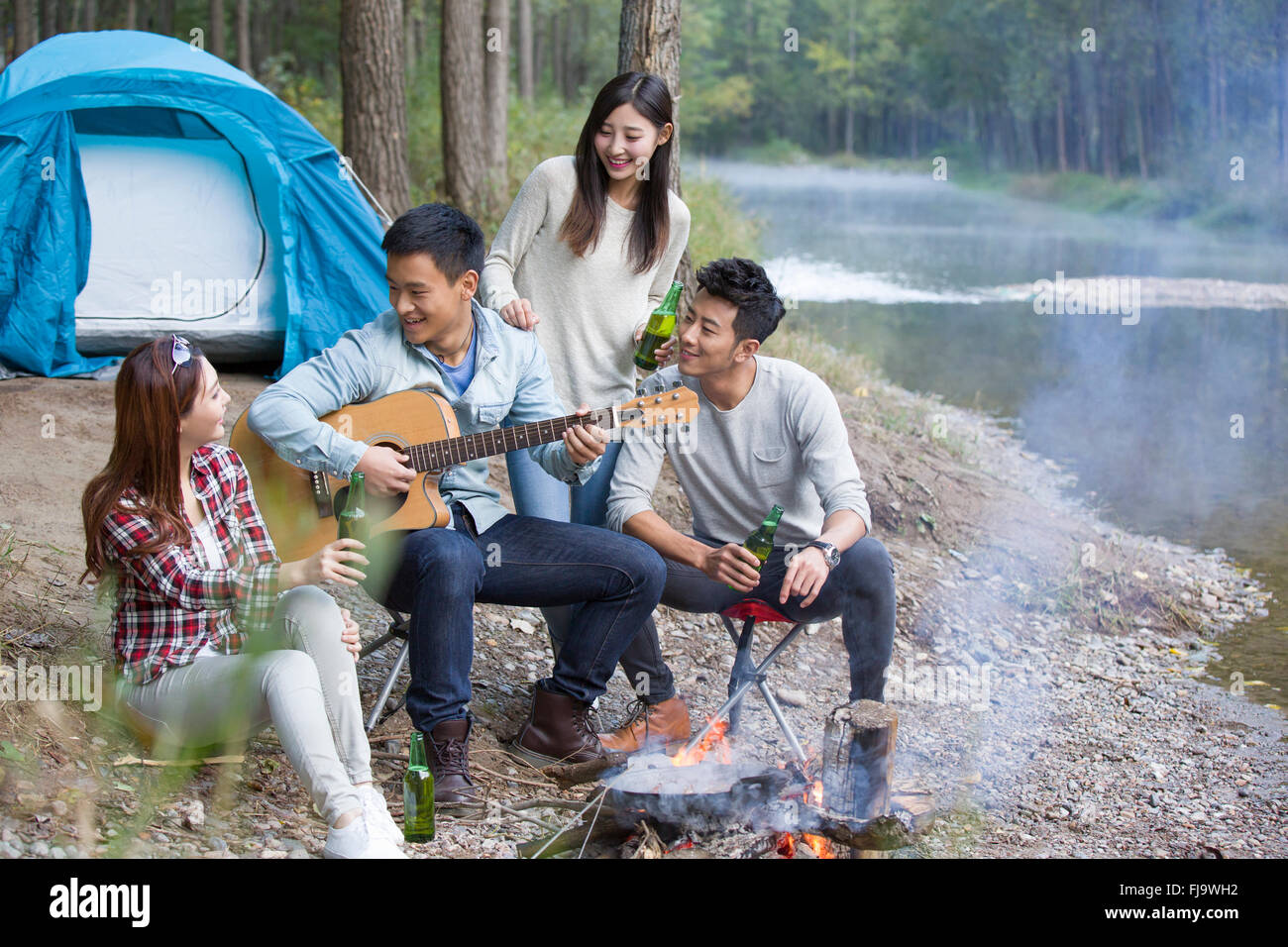 Giovani amici cinesi seduti intorno al fuoco a suonare la chitarra Foto Stock