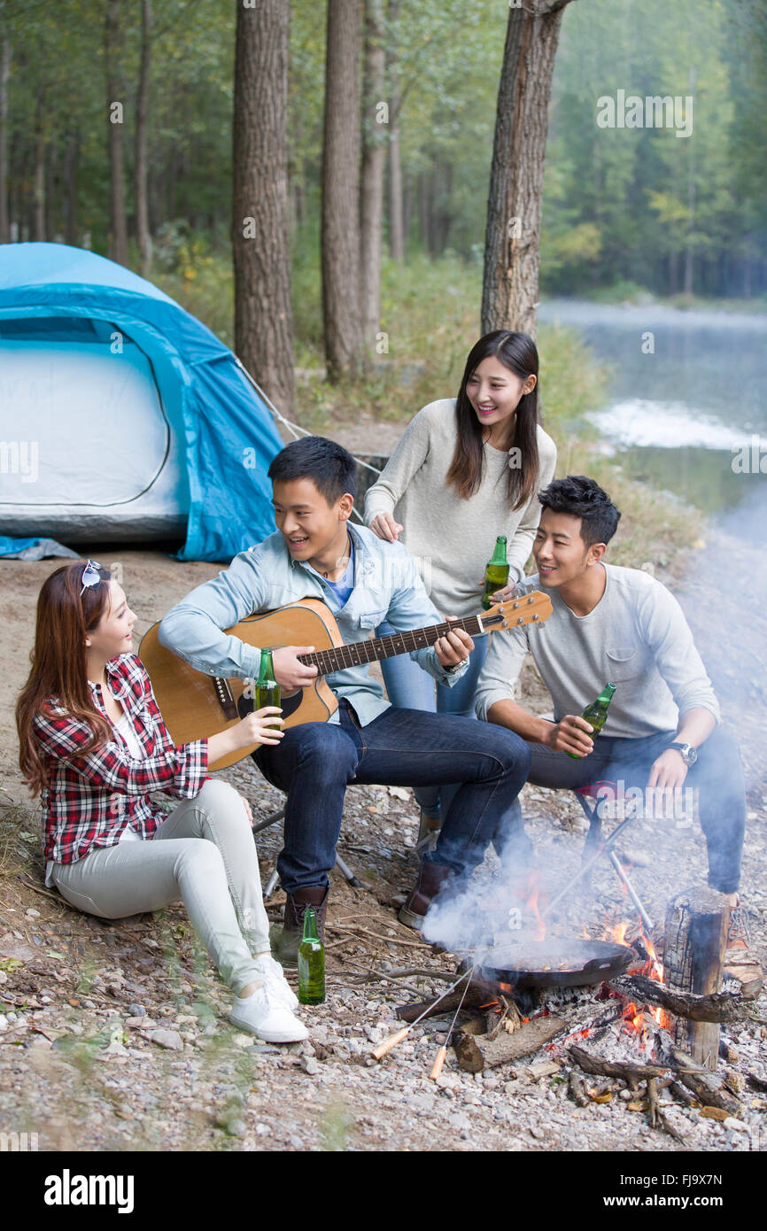 Giovani amici cinesi seduti intorno al fuoco a suonare la chitarra Foto Stock