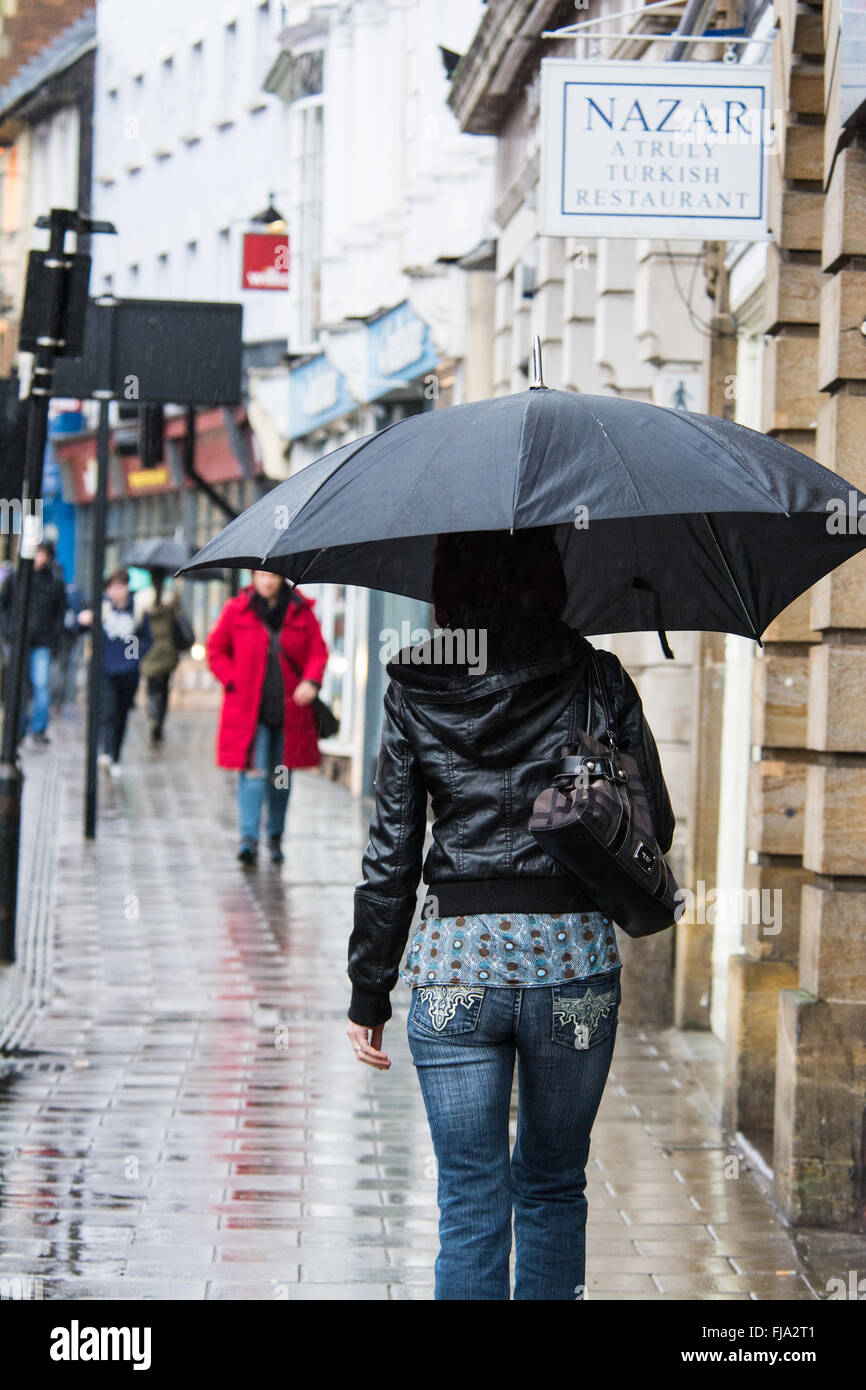 Ragazza con ombrello a camminare su high street sotto la pioggia, Bedford, Bedfordshire Foto Stock
