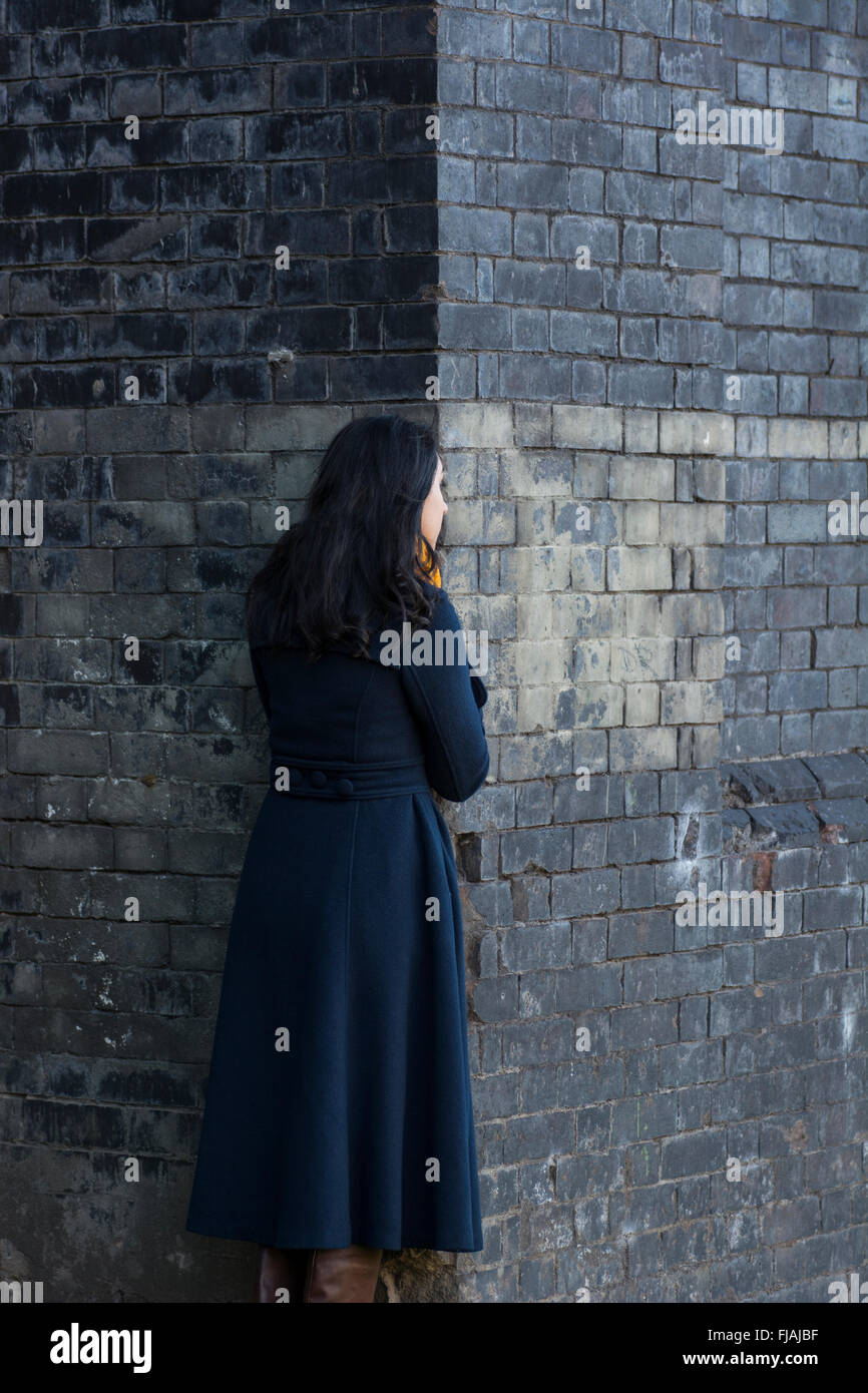 Giovane donna in piedi dietro un muro esterno Foto Stock