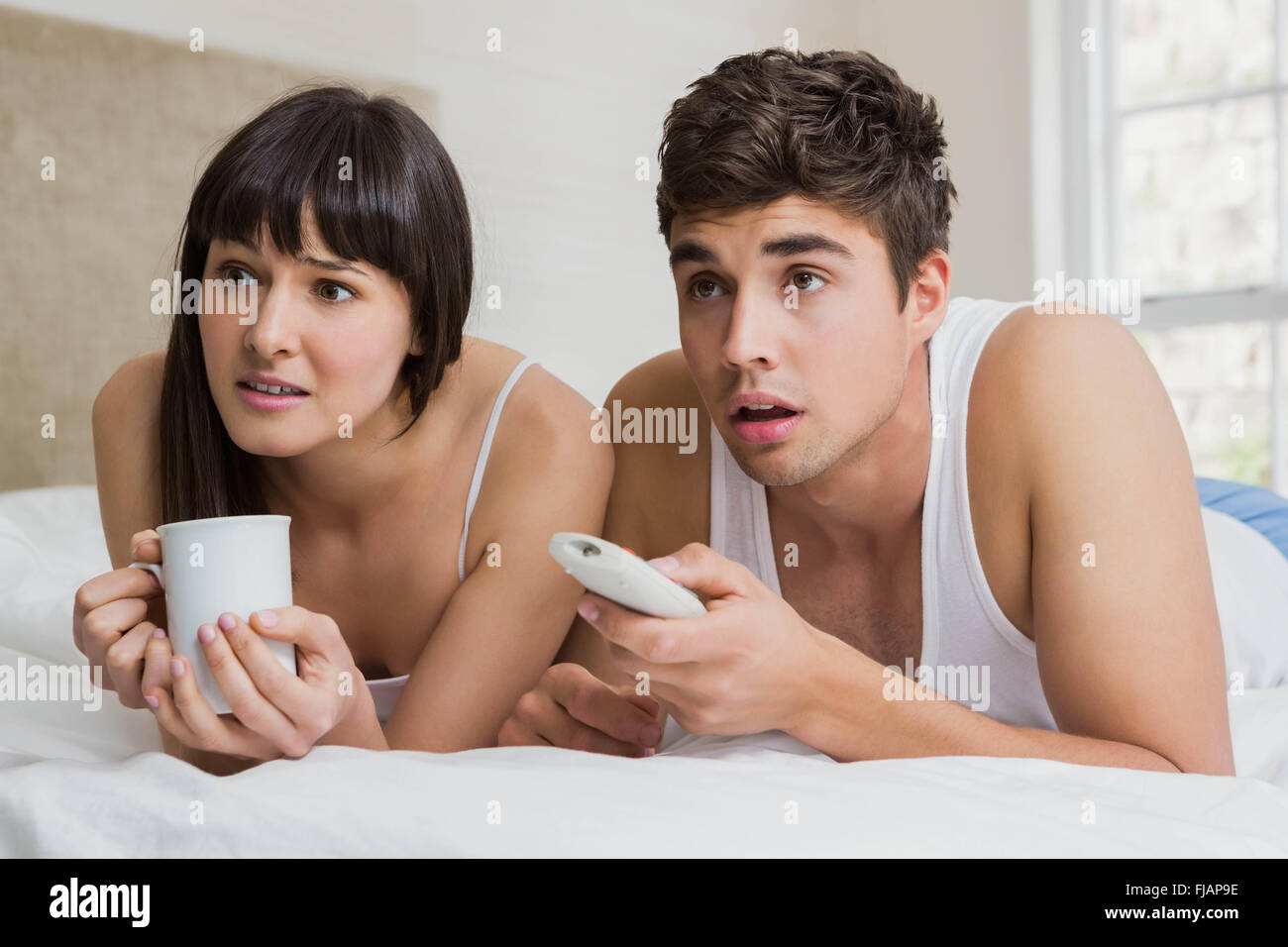 Coppia giovane guardando la televisione insieme sul letto Foto Stock