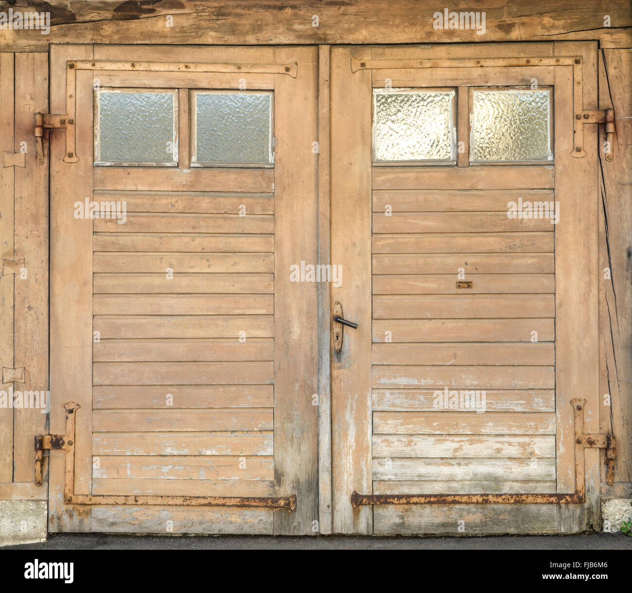 Vecchio, marrone chiaro, sporco e stagionato garage in legno porta con quattro piccole finestre di vetro e ferro forgiato i raccordi. Foto Stock