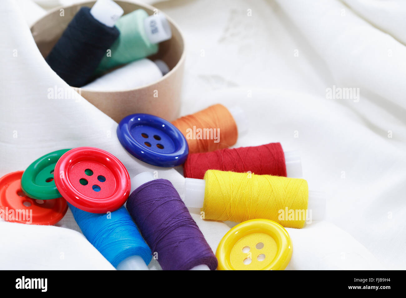 Set di filettatura colorato e pulsanti sul tessile bianco Foto Stock