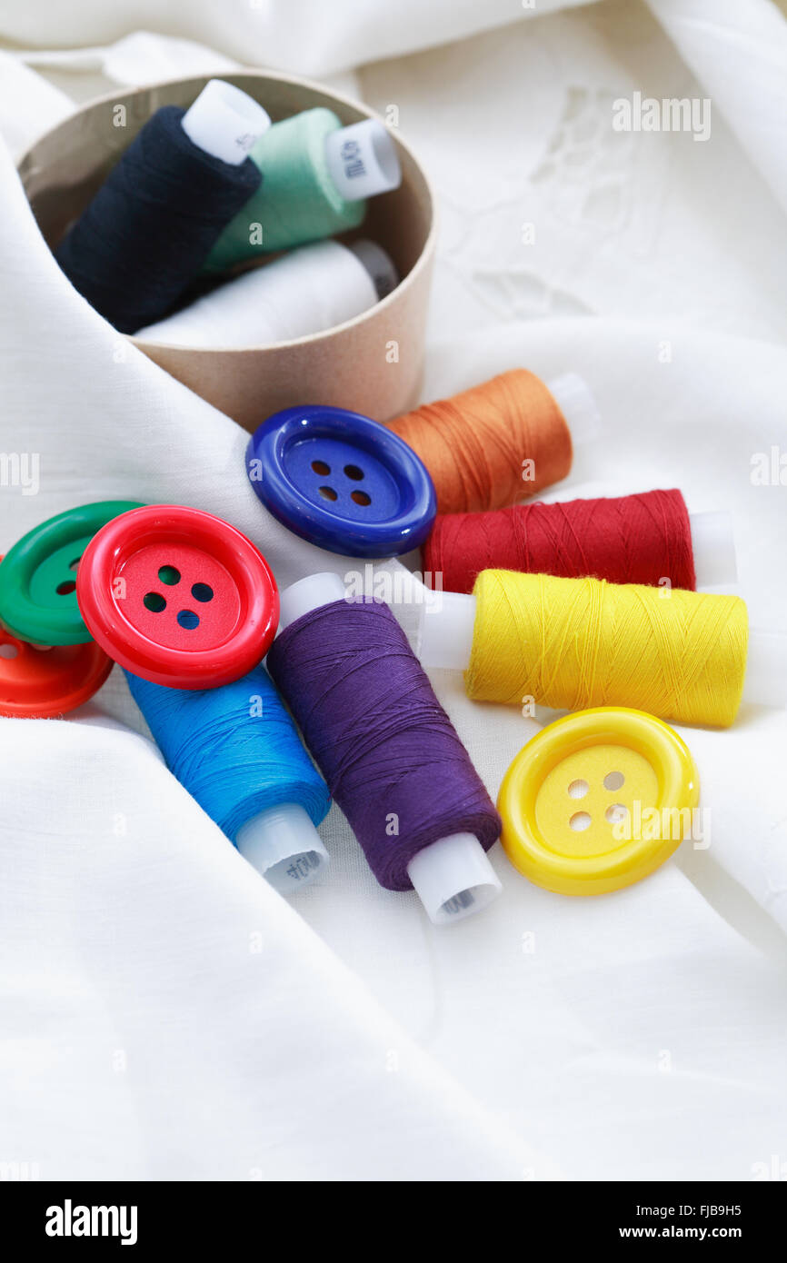 Set di filettatura colorato e pulsanti sul tessile bianco Foto Stock