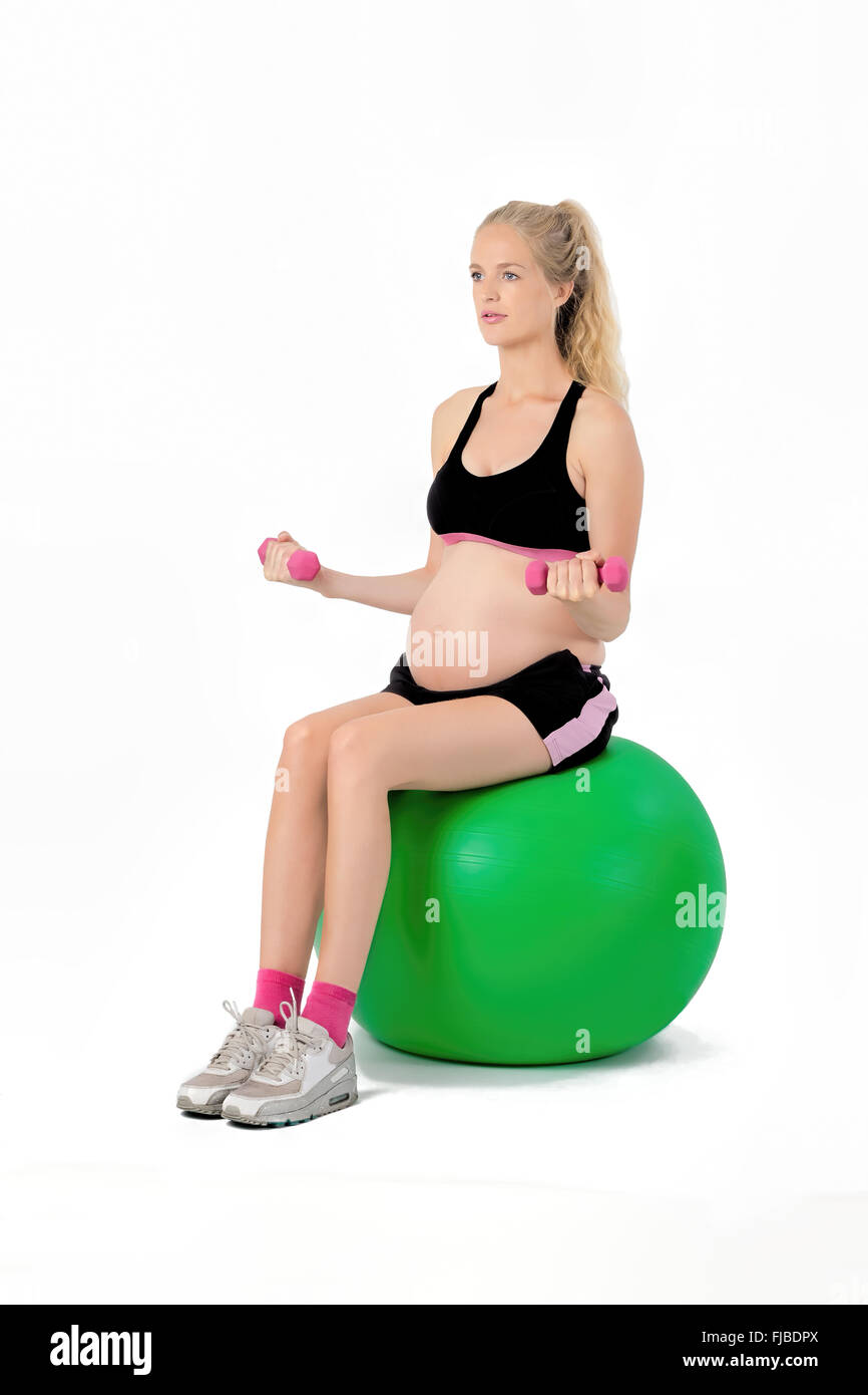 Donna incinta sul saldo di yoga palla eseguendo bicipite curl esercizio con pesi. Foto Stock