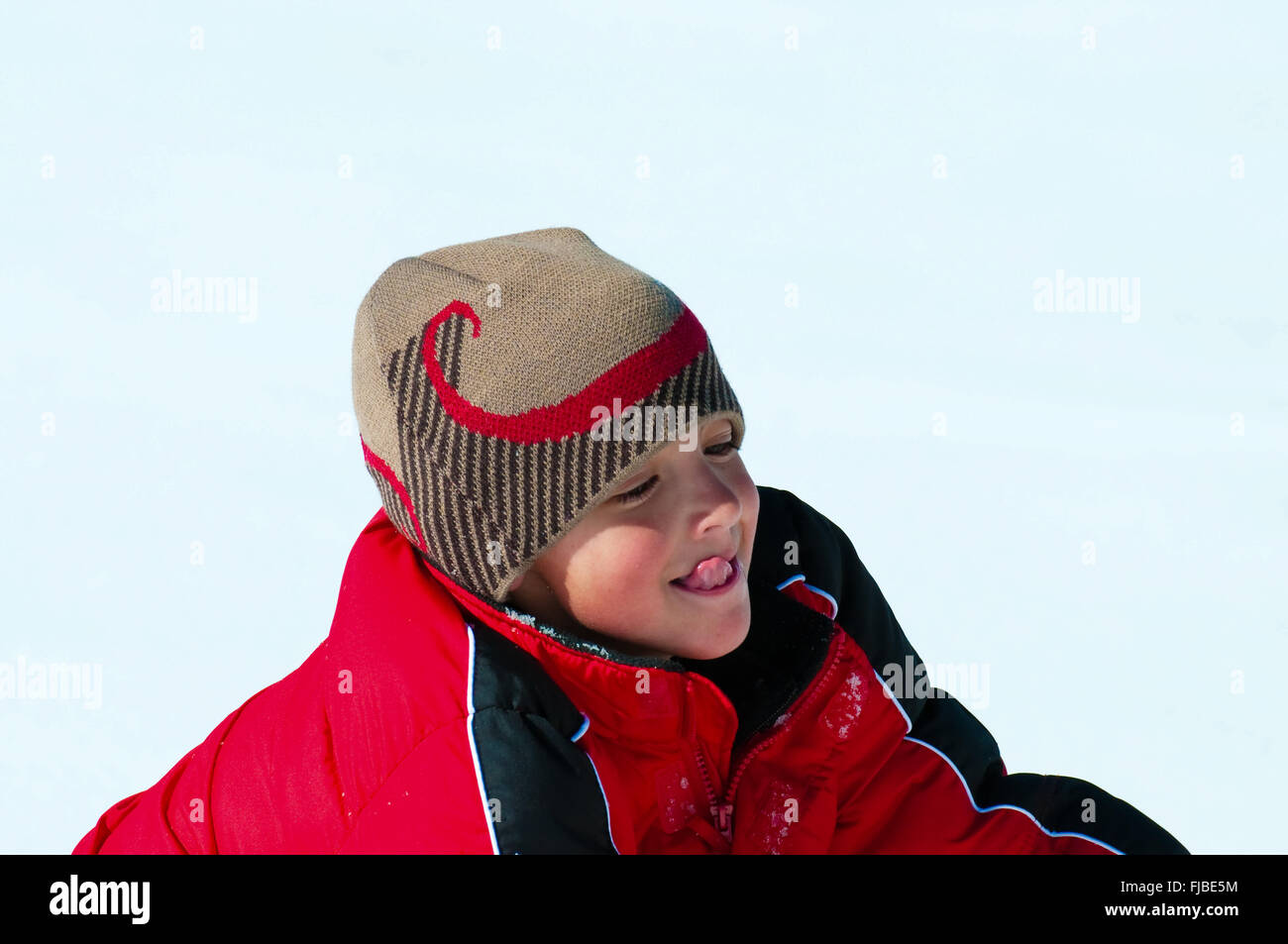 Close-up di adorabili ragazzo con la lingua fuori a giocare nella neve indossando un cappotto rosso. Foto Stock