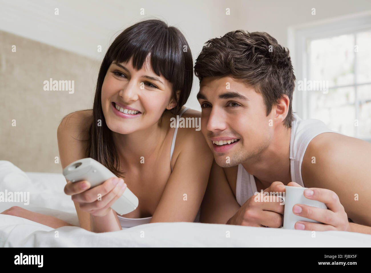 Coppia giovane guardando la televisione insieme sul letto Foto Stock