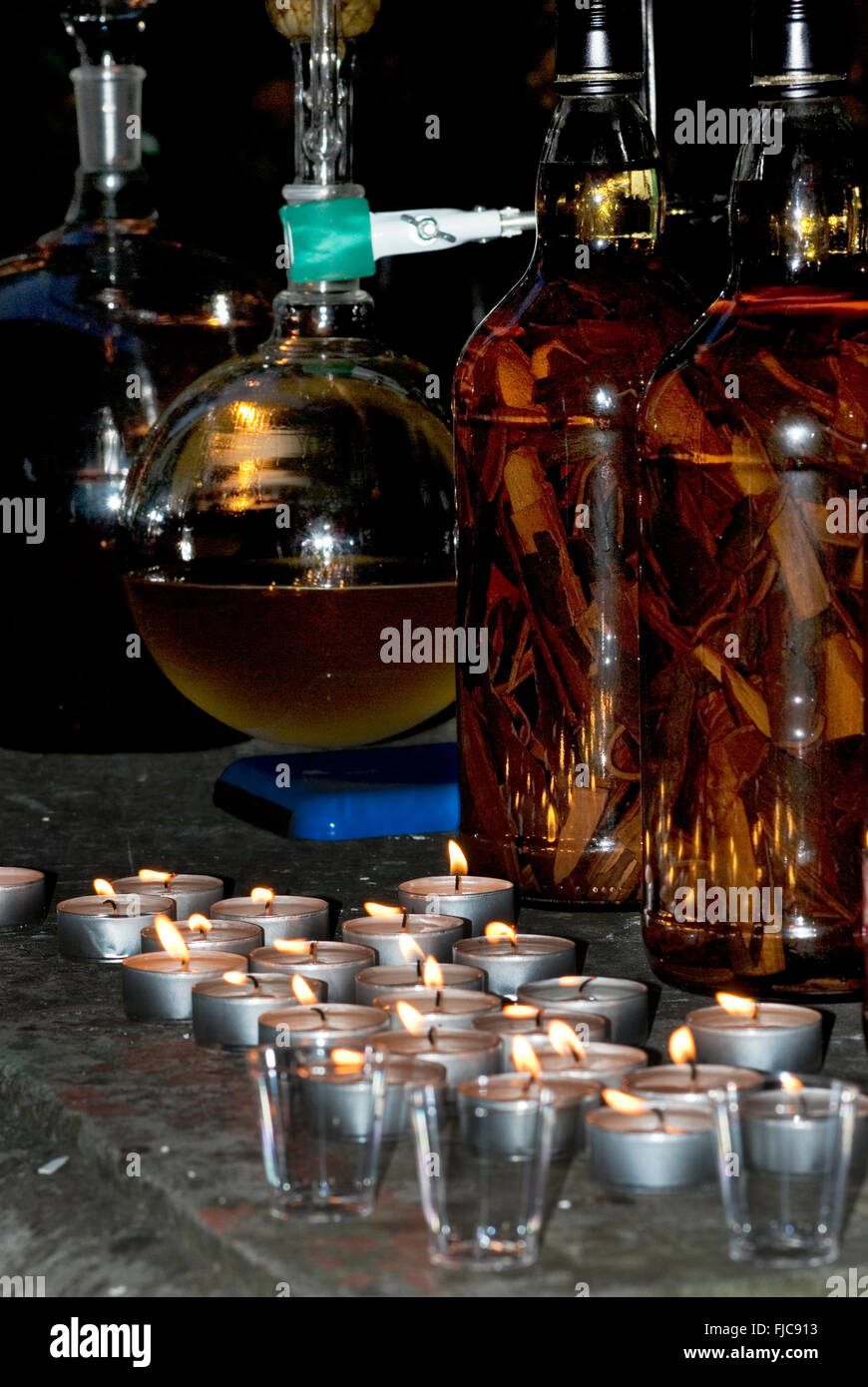 Il gin distillery ancora fuori dal lume di candela, con bacche di ginepro, palloni di vetro, tubi, luci fairy & spezie Foto Stock