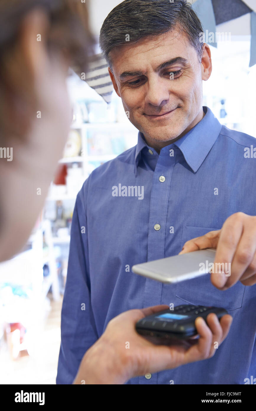 Uomo che utilizza il pagamento senza contatto App sul telefono cellulare in negozio Foto Stock