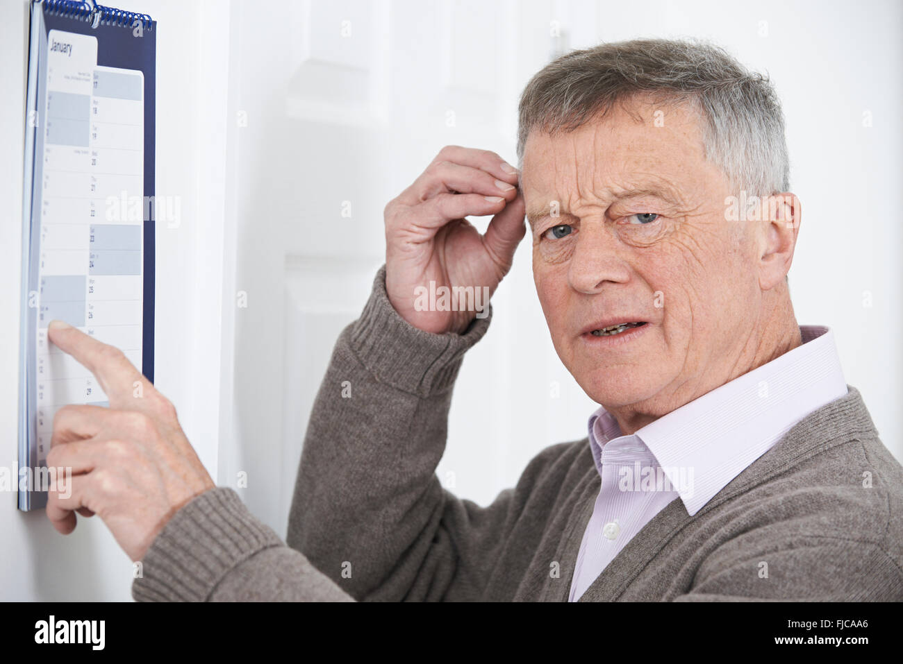 Confuso uomo anziano con demenza guardando il calendario da parete Foto Stock