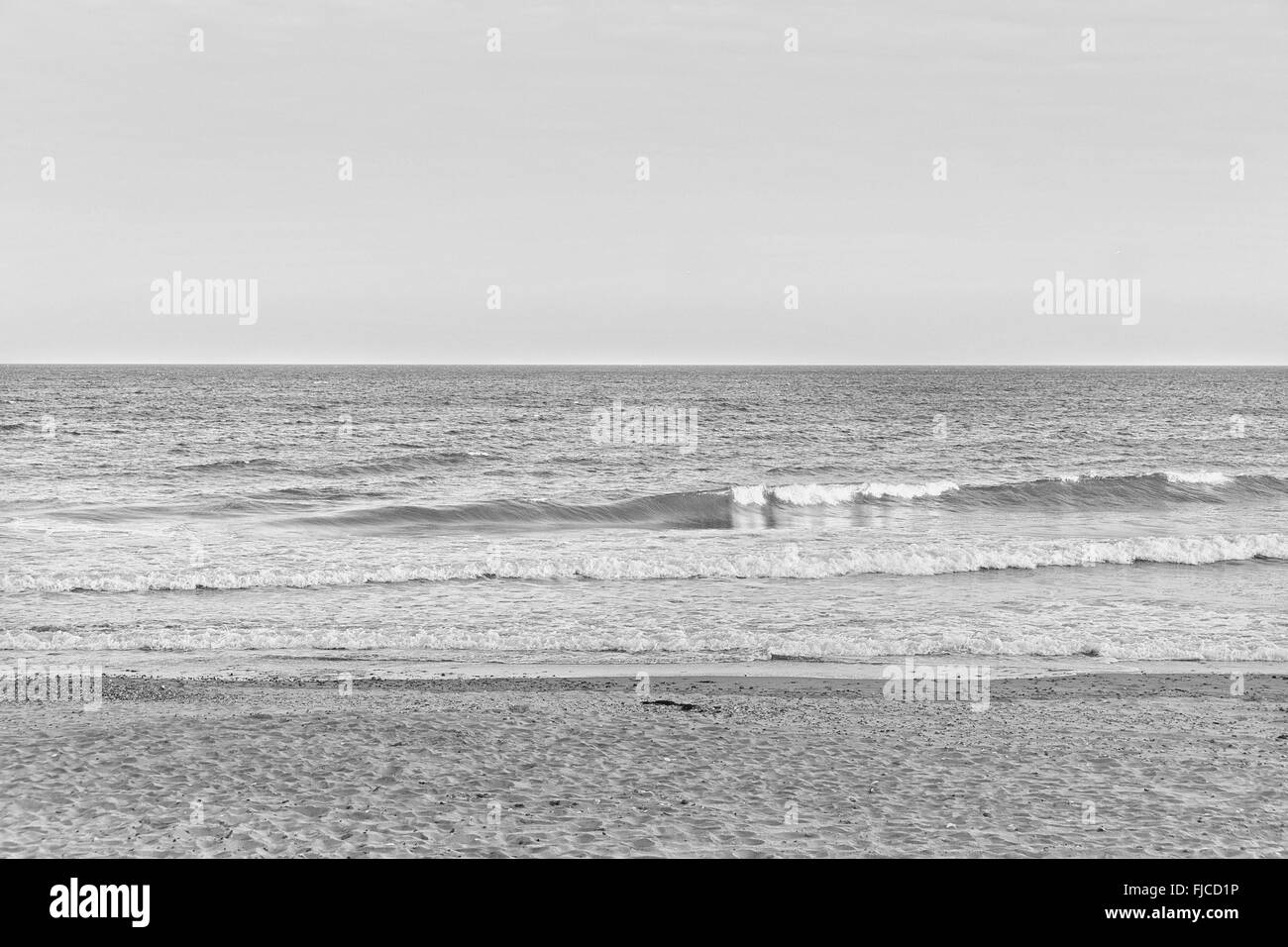 Una immagine in bianco e nero di un'estate la luce del tramonto, guardando le onde in spiaggia con sabbia e una non nuvole nel cielo in EUR Foto Stock