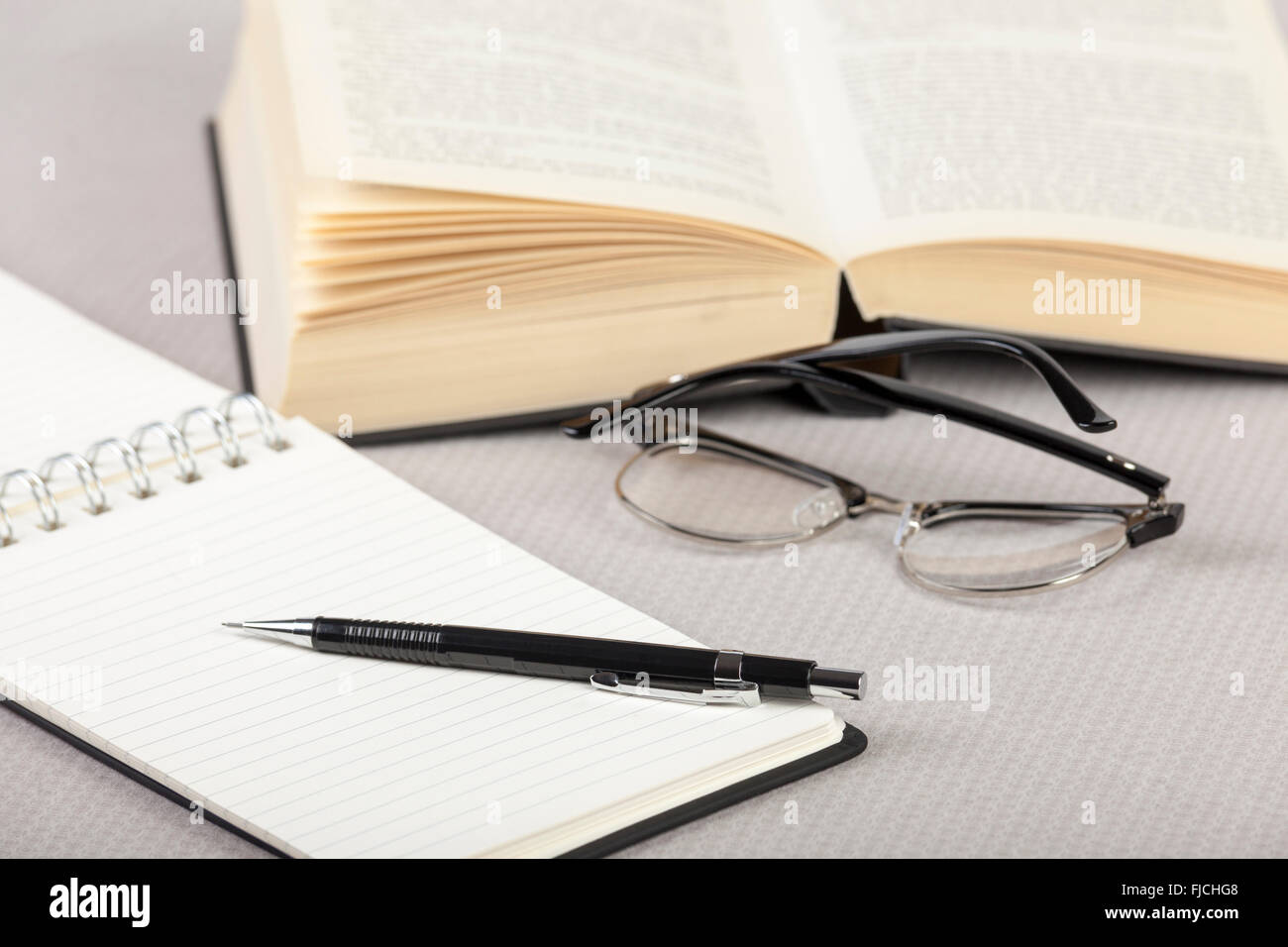 Blocco note e penna su un tavolo con un libro aperto e un paio di occhiali Foto Stock