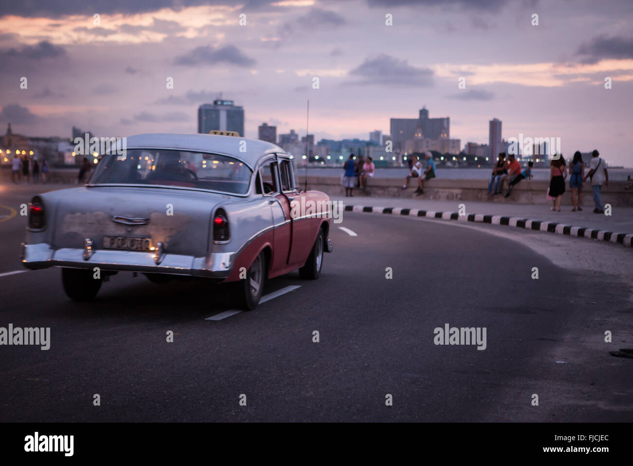 L'Avana, Cuba. Un auto d'epoca passeggiate lungo Malecòn, il lungomare della città, al tramonto. Foto Stock
