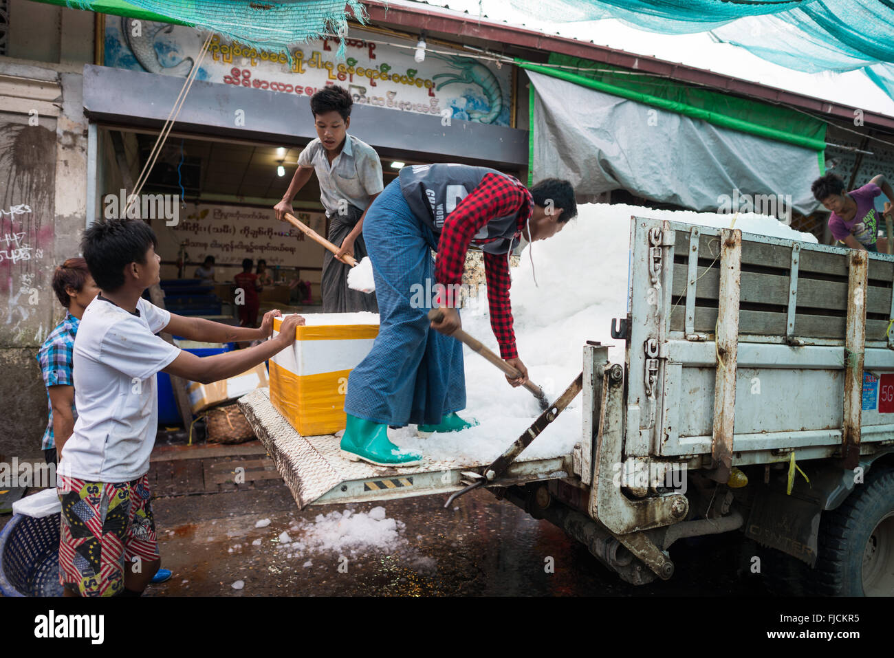 Ice Delivery Fish Market Mandalay Myanmar // MANDALAY, Myanmar — gli uomini spalmano il ghiaccio dal retro di un camion in secchi e refrigeratori per la consegna ai venditori di pesce al mercato di pesci e fiori vicino a Pulaing Street a Mandalay. Il sistema di consegna del ghiaccio supporta le attività quotidiane dei venditori ambulanti che si affidano alla refrigerazione per preservare i loro prodotti ittici nel clima tropicale del Myanmar. Mandalay, la seconda città più grande del paese ed ex capitale reale, funge da importante centro commerciale nel Myanmar centrale. I mercati tradizionali della città rimangono centri vitali del commercio locale, collegando i professionisti rurali Foto Stock