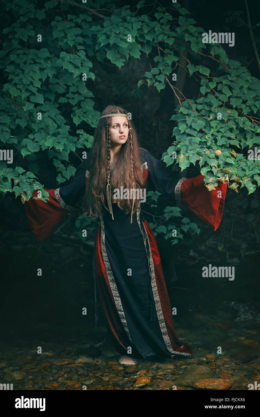 Bella giovane donna con abito medievale in un flusso di foresta Foto Stock