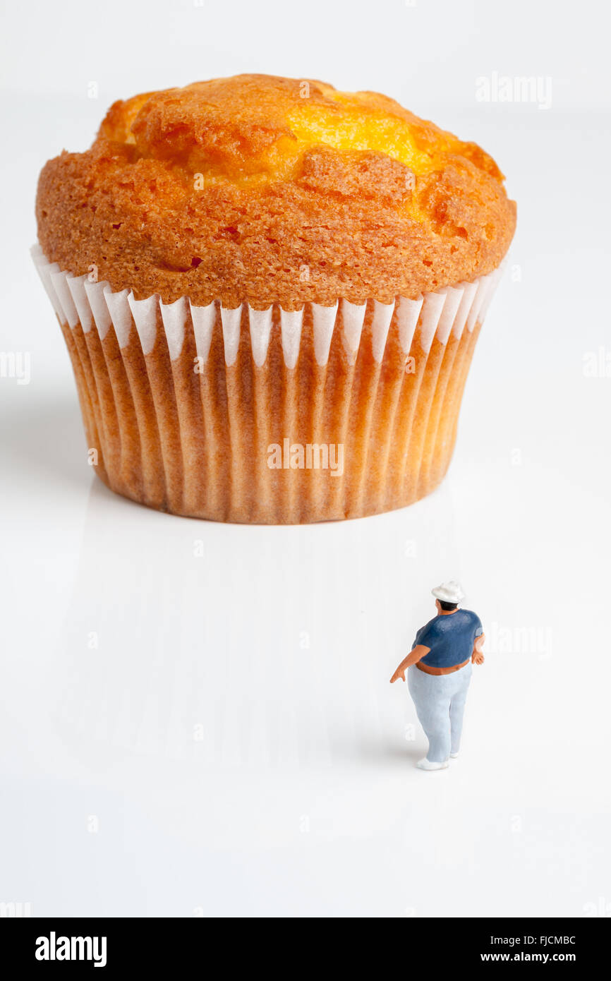 Il sovrappeso man looking fino ad un enorme muffin grandi una porzione di dimensioni o di concetto di obesità Foto Stock