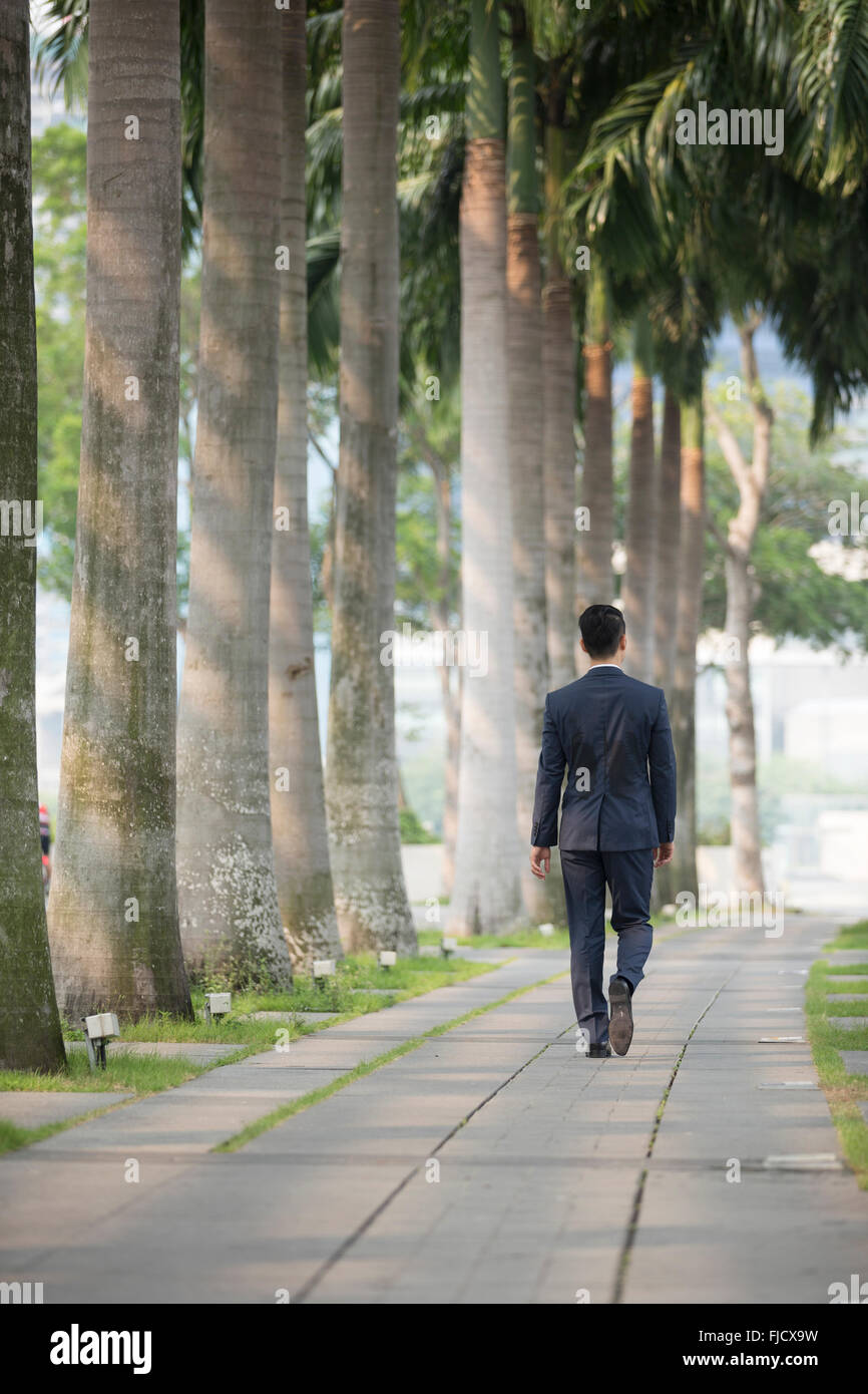 Business cinese uomo a camminare per la strada con il suo ritorno alla fotocamera Foto Stock