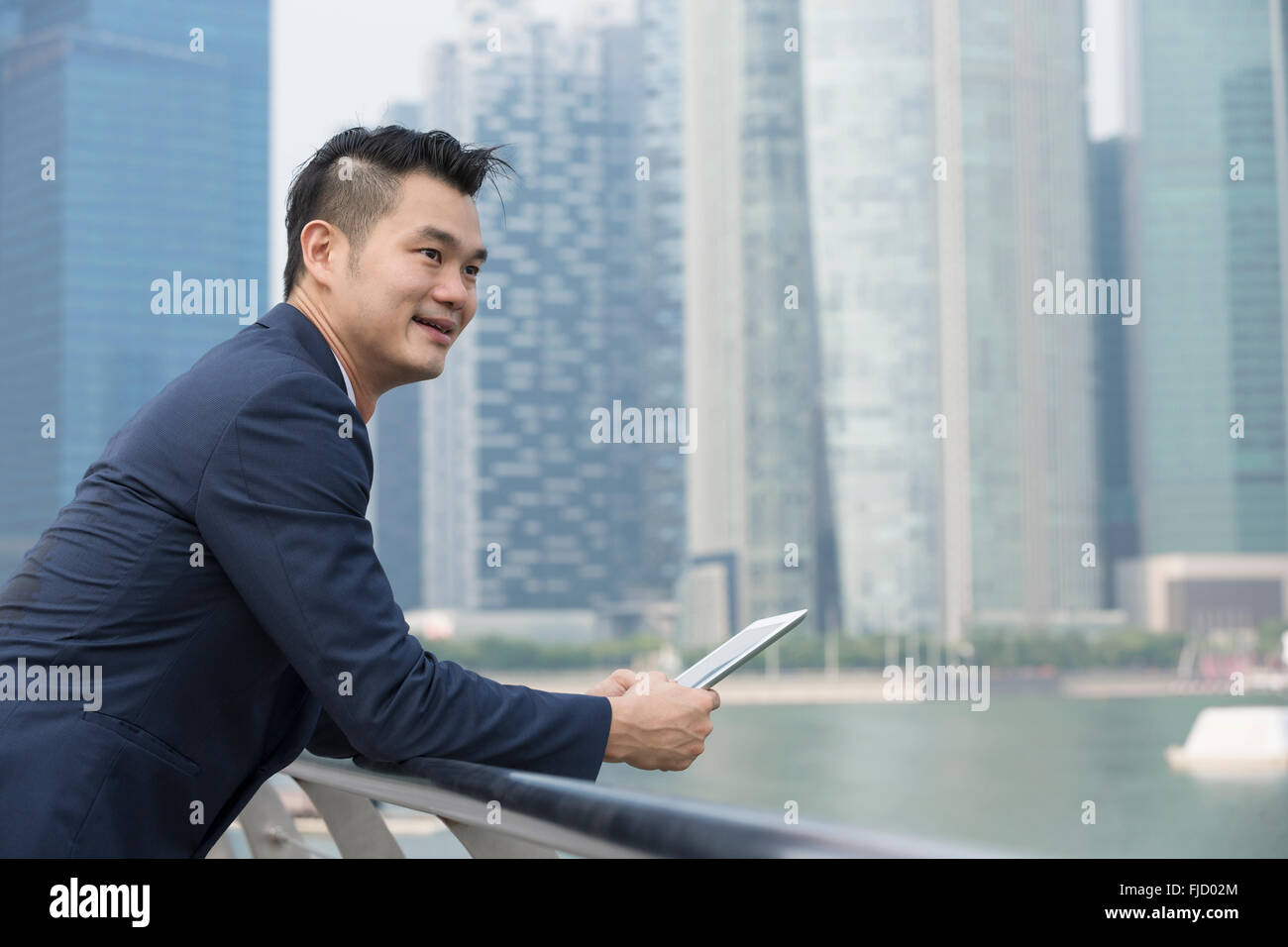 Uomo cinese con un computer tablet. Asian business man tenere una tavoletta digitale computer, in piedi di fronte a un grattacielo. Foto Stock