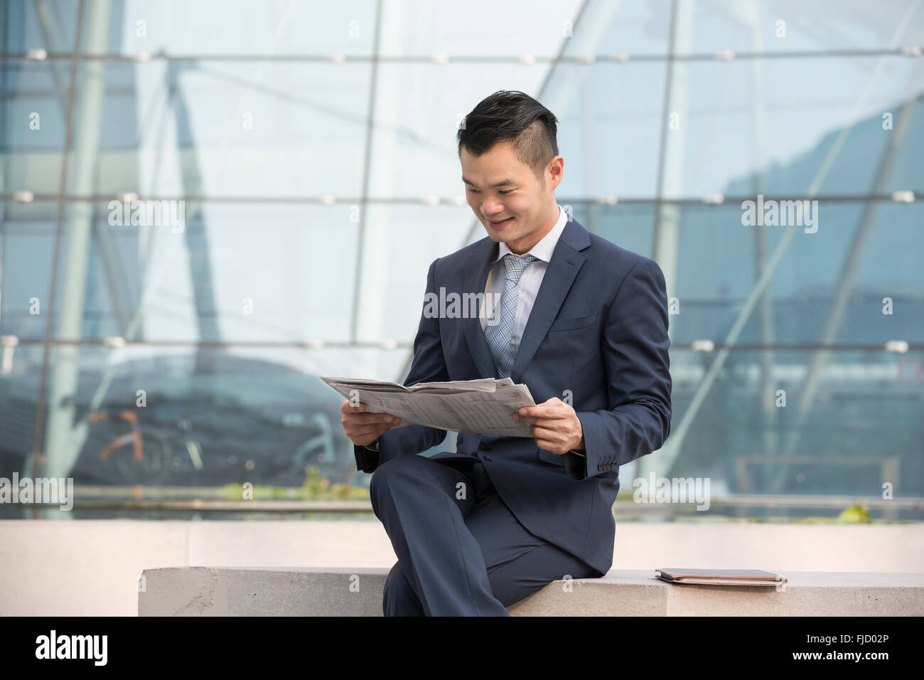 Chinese Business man al di fuori ufficio leggendo un giornale. Asian business uomo prendendo una pausa. Foto Stock