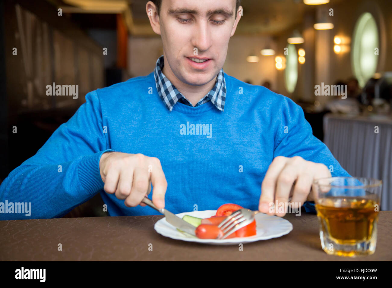 Ritratto di giovane sorridente uomo in interni di mangiare le verdure con la salsiccia con coltello e forchetta Foto Stock