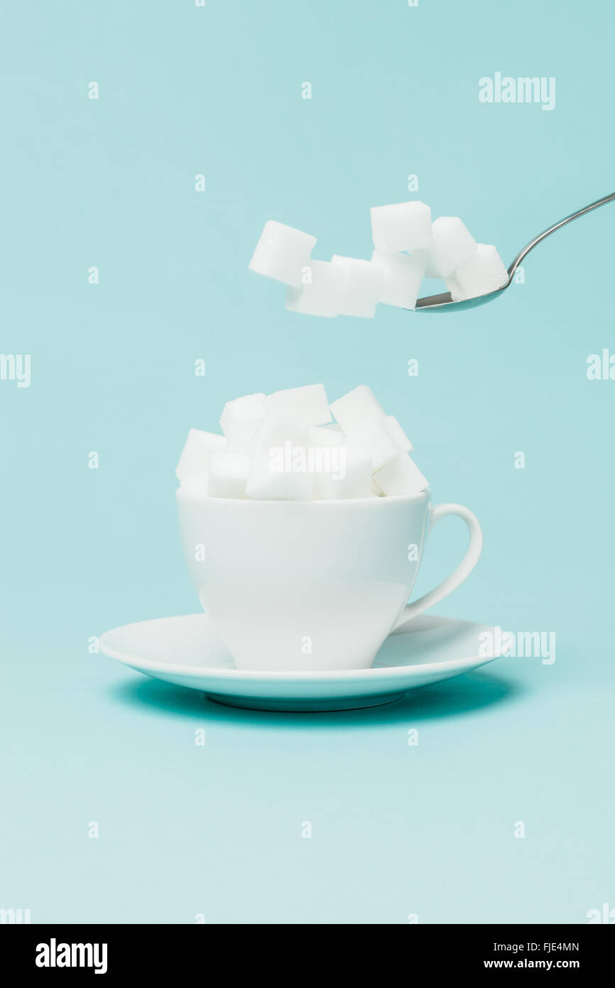 Aggiunta di una quantità eccessiva di zucchero in una tazza di tè. Foto Stock