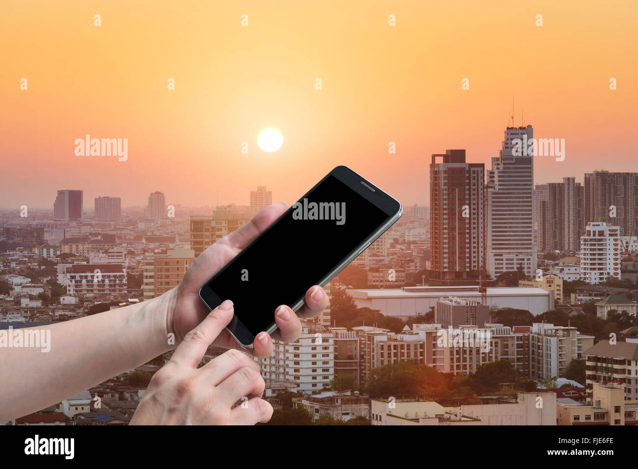 Femmina di tenere in mano e il touch screen smart phone, tablet,cellulare sulla città della luce del sole sullo sfondo. Foto Stock