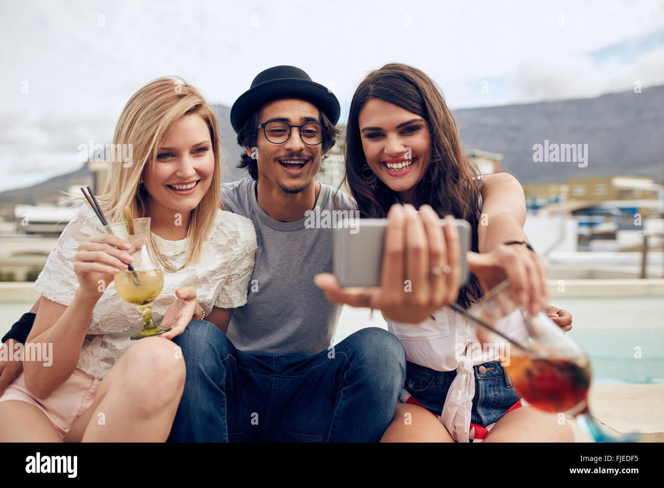 Gruppo di amici prendendo selfie su uno smart phone. Giovane uomo e donna con drink prendendo un autoritratto sul telefono cellulare. Giovani peo Foto Stock