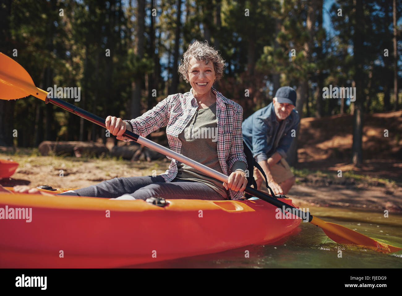 Ritratto di felice donna senior in un kayak le piastre di contenimento. Donna canoa con l uomo in fondo al lago. Foto Stock