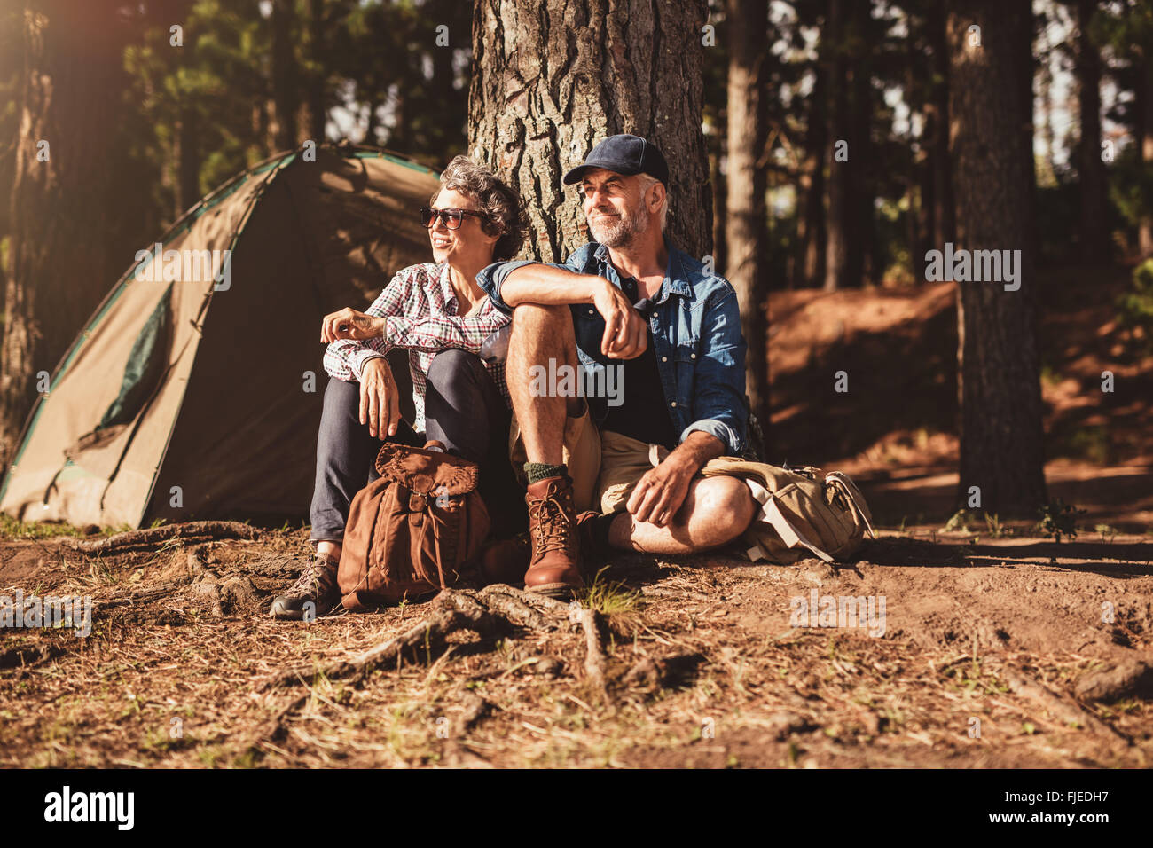 Ritratto di coppia senior seduti insieme sotto un albero nella foresta e guardando a una vista. Uomo maturo e la donna in un momento di relax a loro Foto Stock