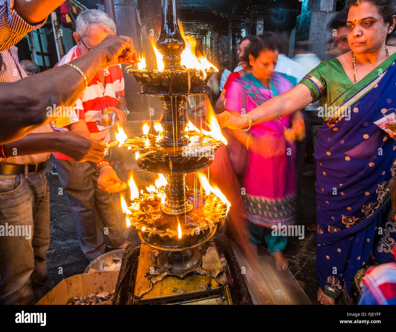 Gli indù versando olio su di una fiamma sacra a un tempio in Udupi, nell India meridionale Foto Stock