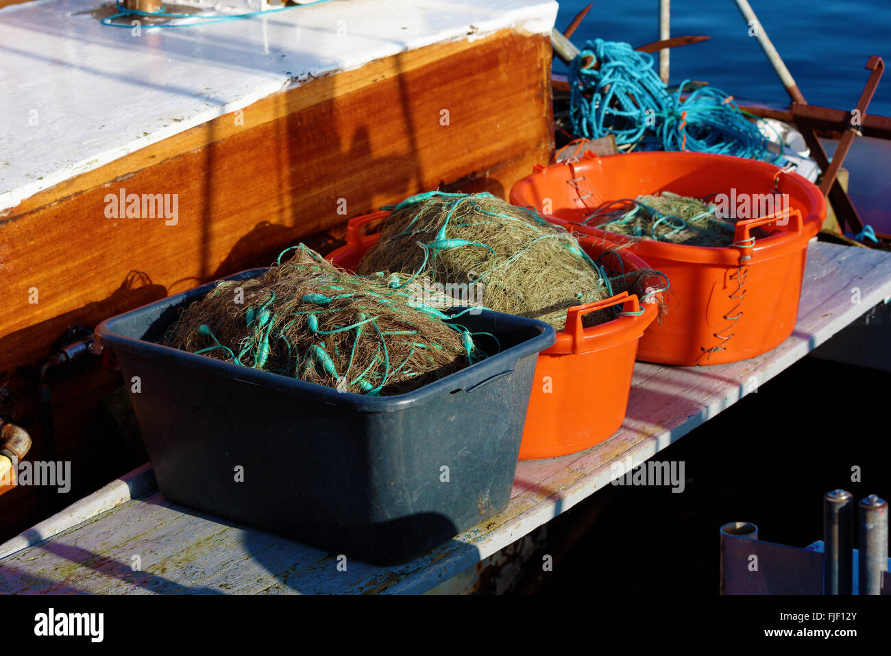 Tre cassette di plastica riempiti con reti da pesca su una piccola barca da pesca. Foto Stock