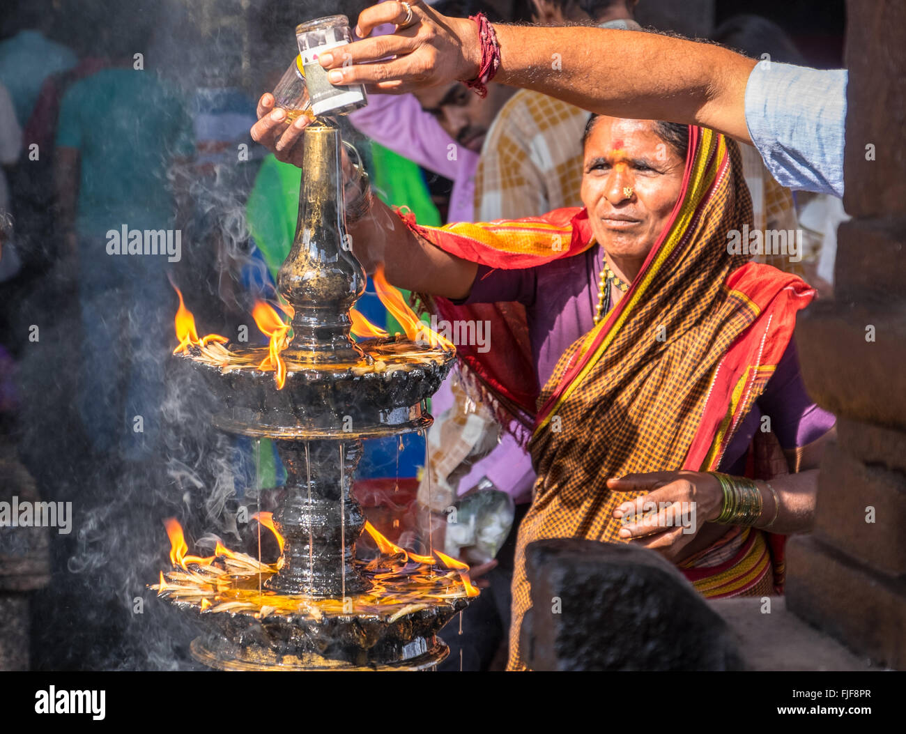 Gli indù versando olio su di una fiamma sacra a un tempio in Udupi, nell India meridionale Foto Stock