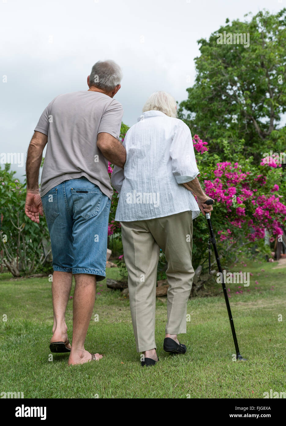 L'uomo aiutando signora anziana con il bastone da passeggio in giardino Foto Stock